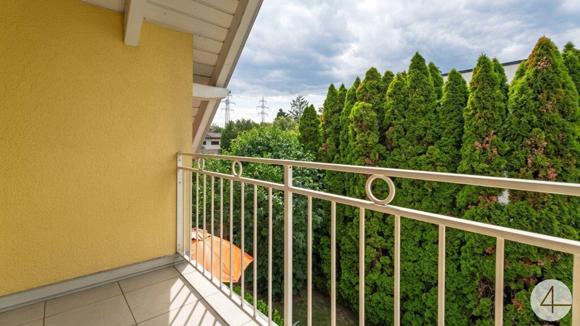Balkon mit Blick auf hohe grüne Bäume und einen bewölkten Himmel.