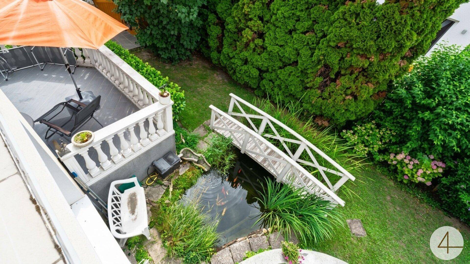 Blick von oben auf den Garten mit Teich, Brücke und einer Terrasse mit Sitzgelegenheiten.