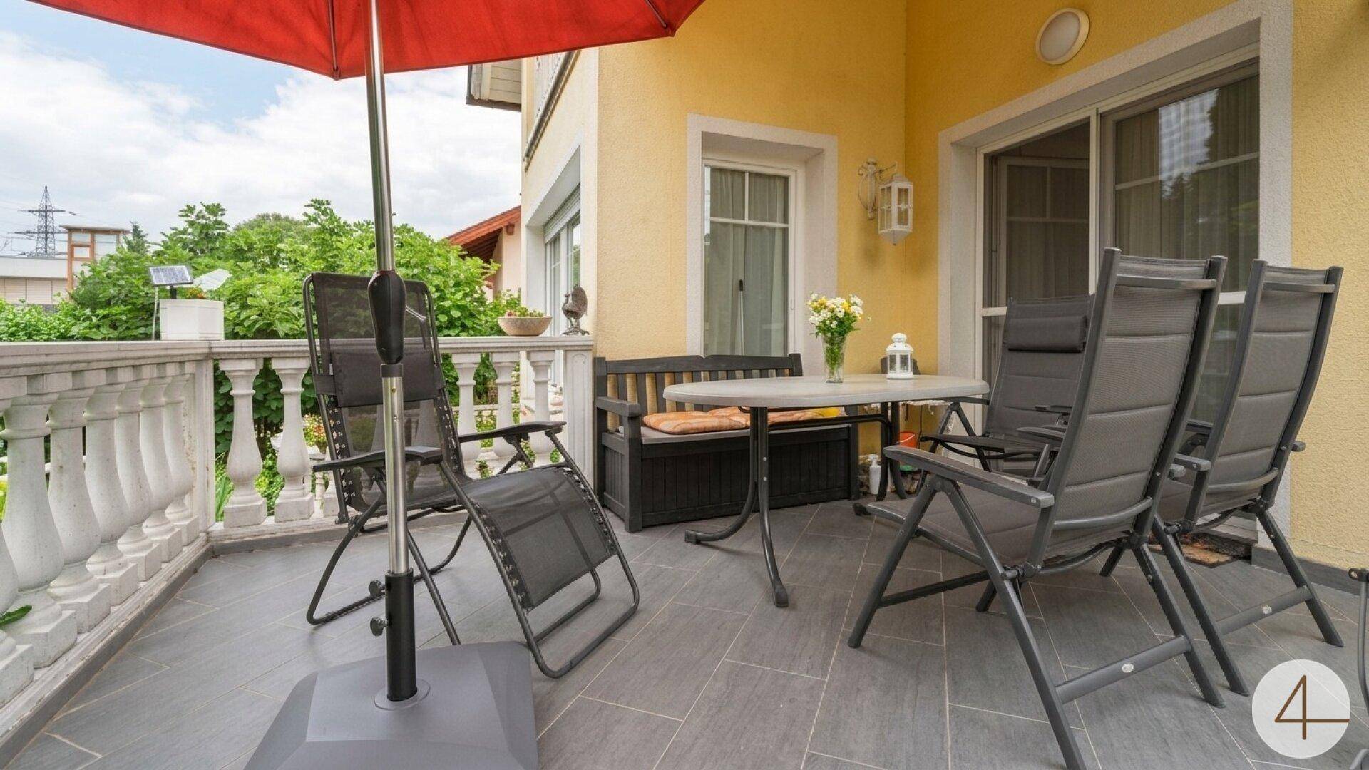 Gemütliche Terrasse mit Gartenmöbeln und rotem Sonnenschirm, direkt am Haus gelegen.