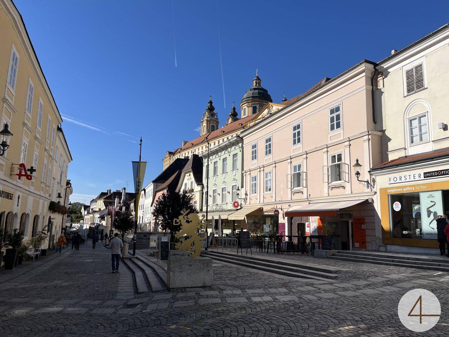 Historische Straße mit vielfältiger Architektur und imposanter Kirchenkuppel im Hintergrund unter klarem Himmel.