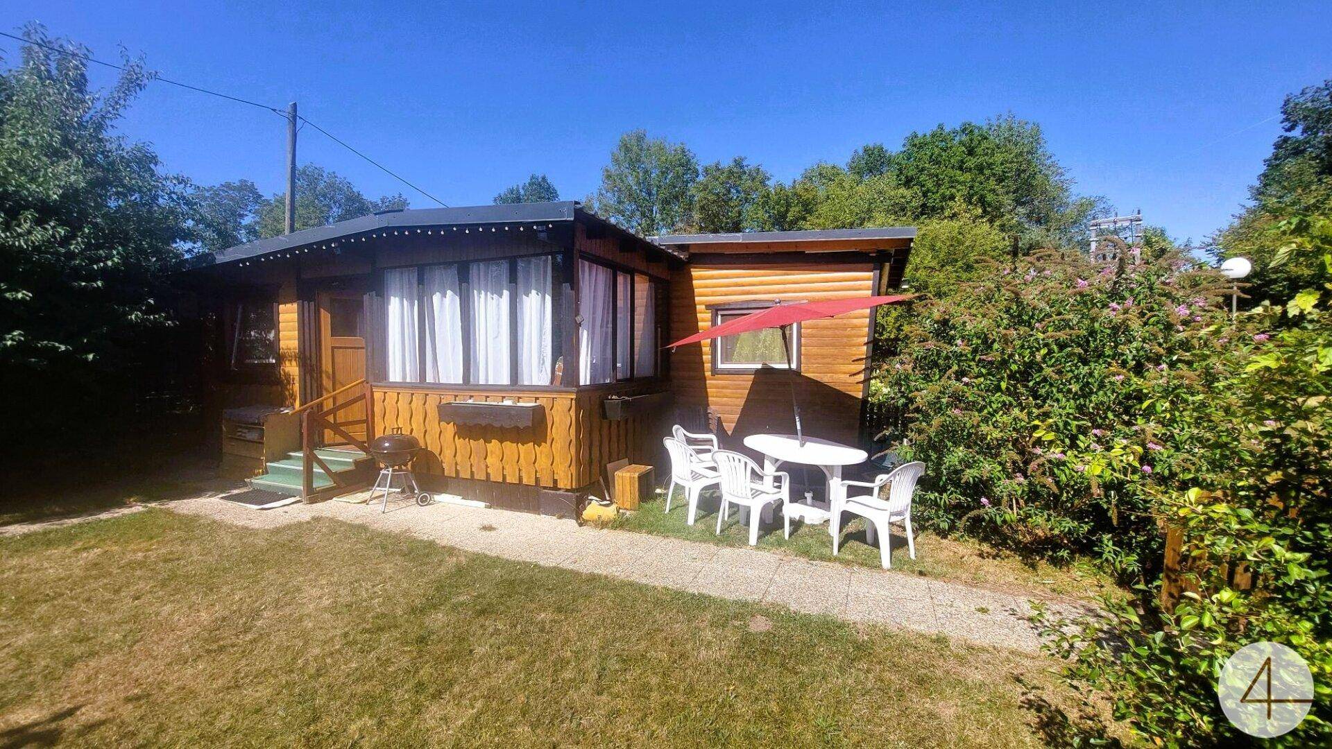 Gemütliches Holzhaus mit Terrasse, Sonnenschirm und Gartenmöbeln auf grünem Rasen.