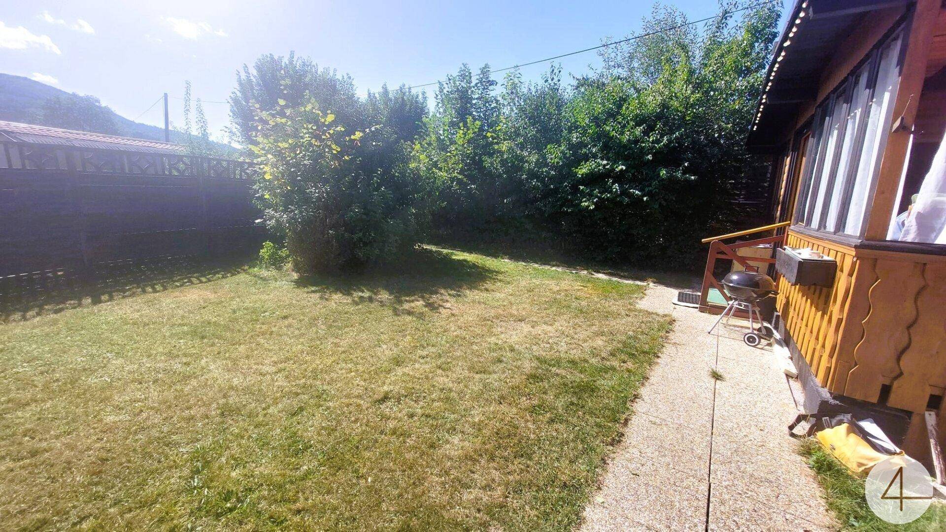 Gepflegter Gartenbereich mit Rasenfläche, Gartenweg und umgebenden Bäumen unter blauem Himmel.