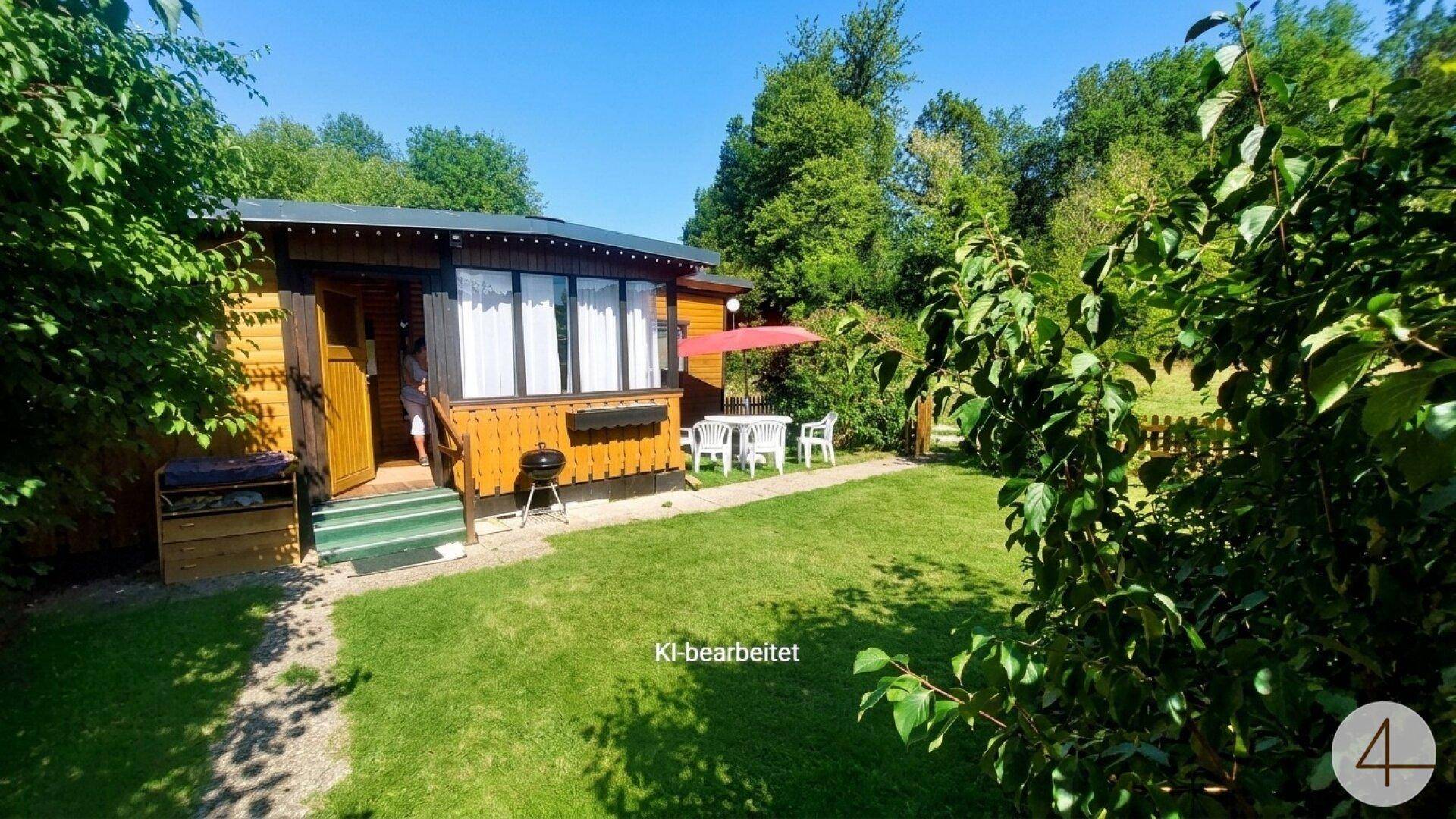Kleines Holzhaus mit gepflegtem Rasen, Grill und Sitzgelegenheiten im Freien an einem sonnigen Tag.