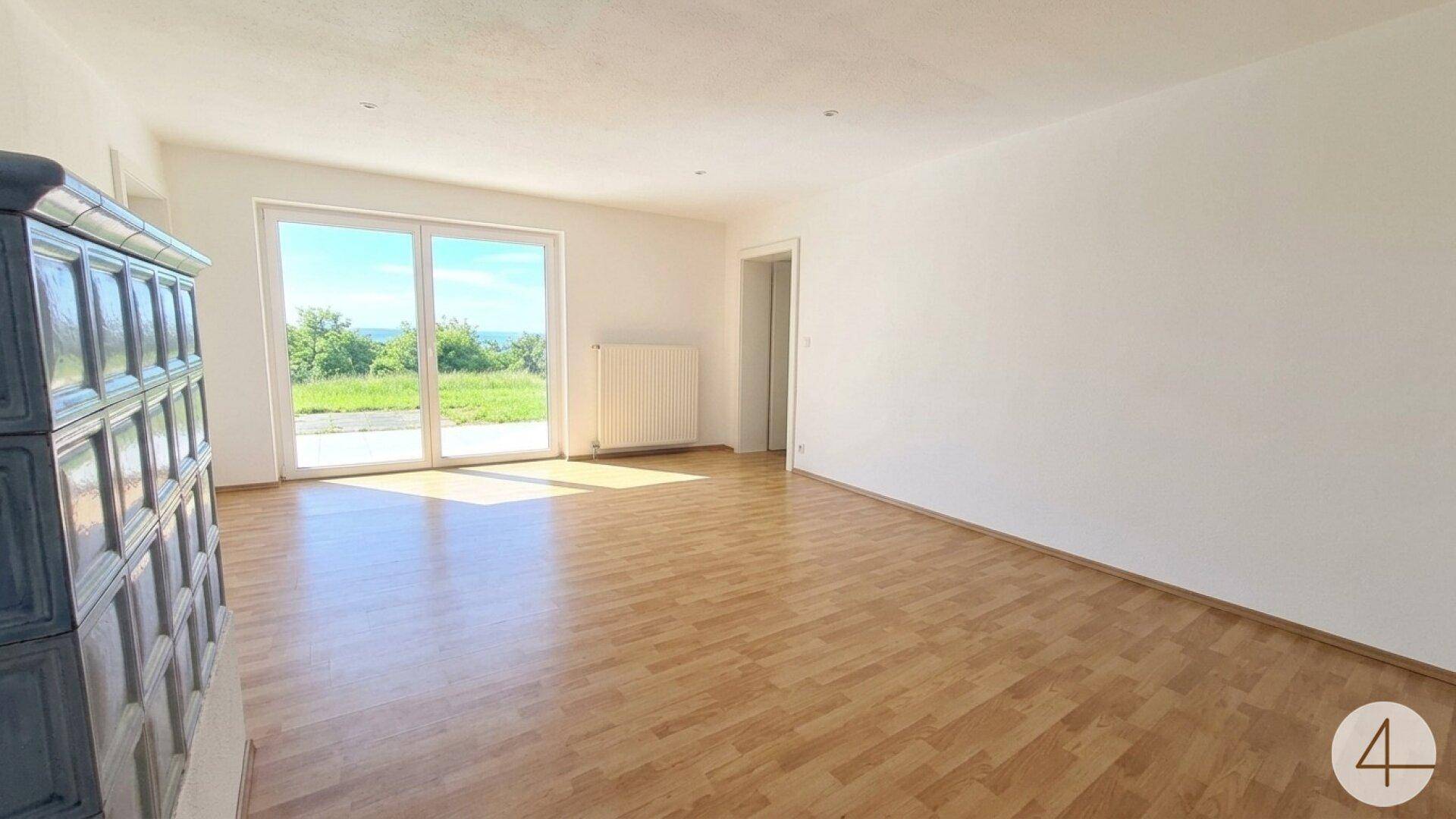 Helles Wohnzimmer mit Laminatboden, großem Fenster und traditionellem Kachelofen.