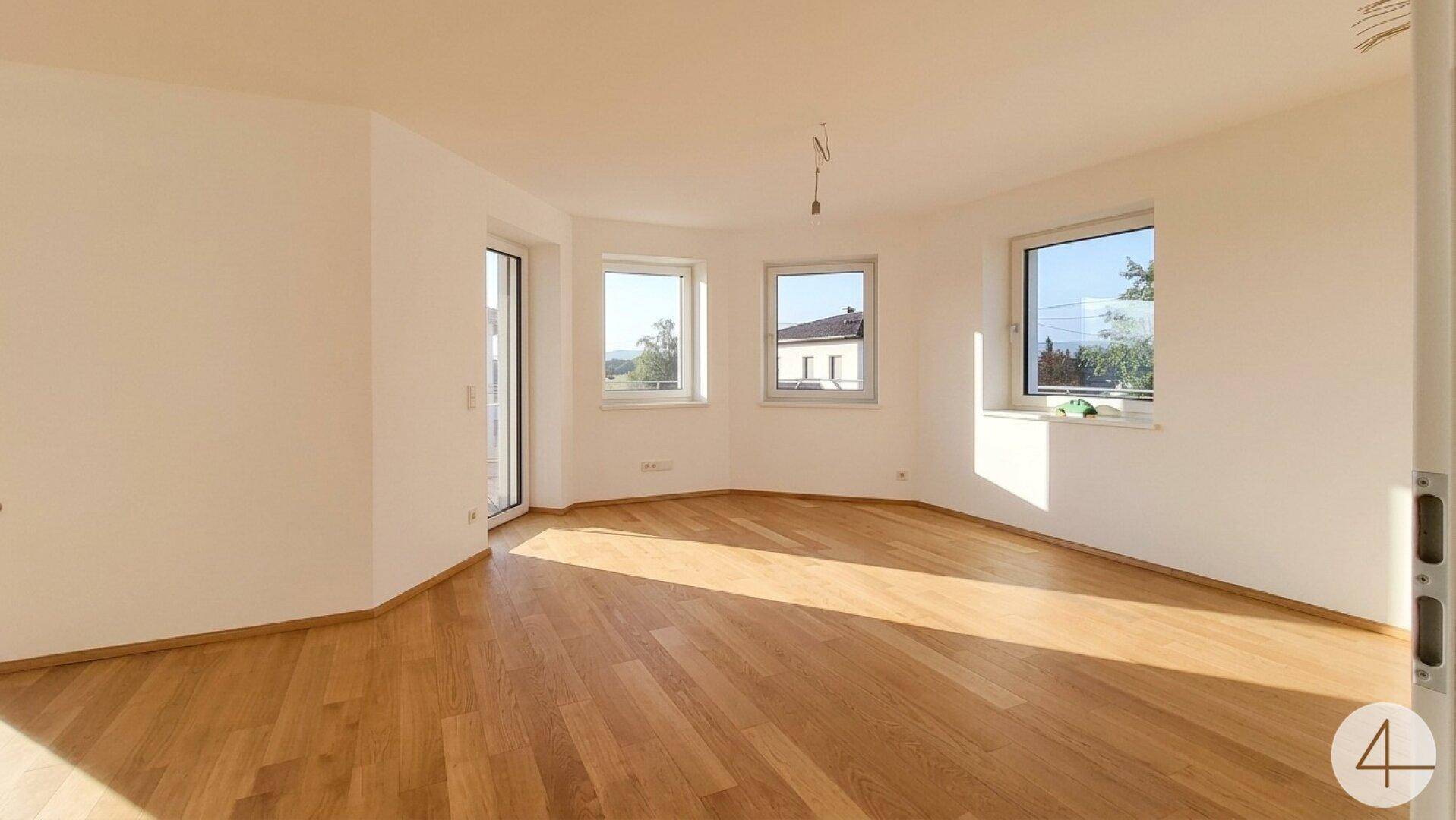 Geräumiger, heller Raum mit Holzboden und großen Fenstern, die viel Tageslicht hereinlassen.