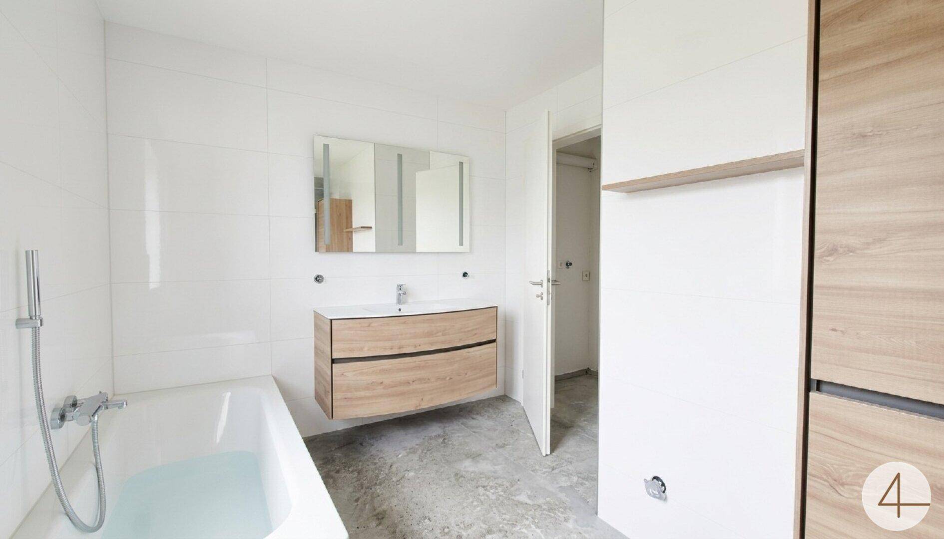 Modernes Badezimmer mit Badewanne, schwebendem Waschtisch und weißen Fliesen an den Wänden.