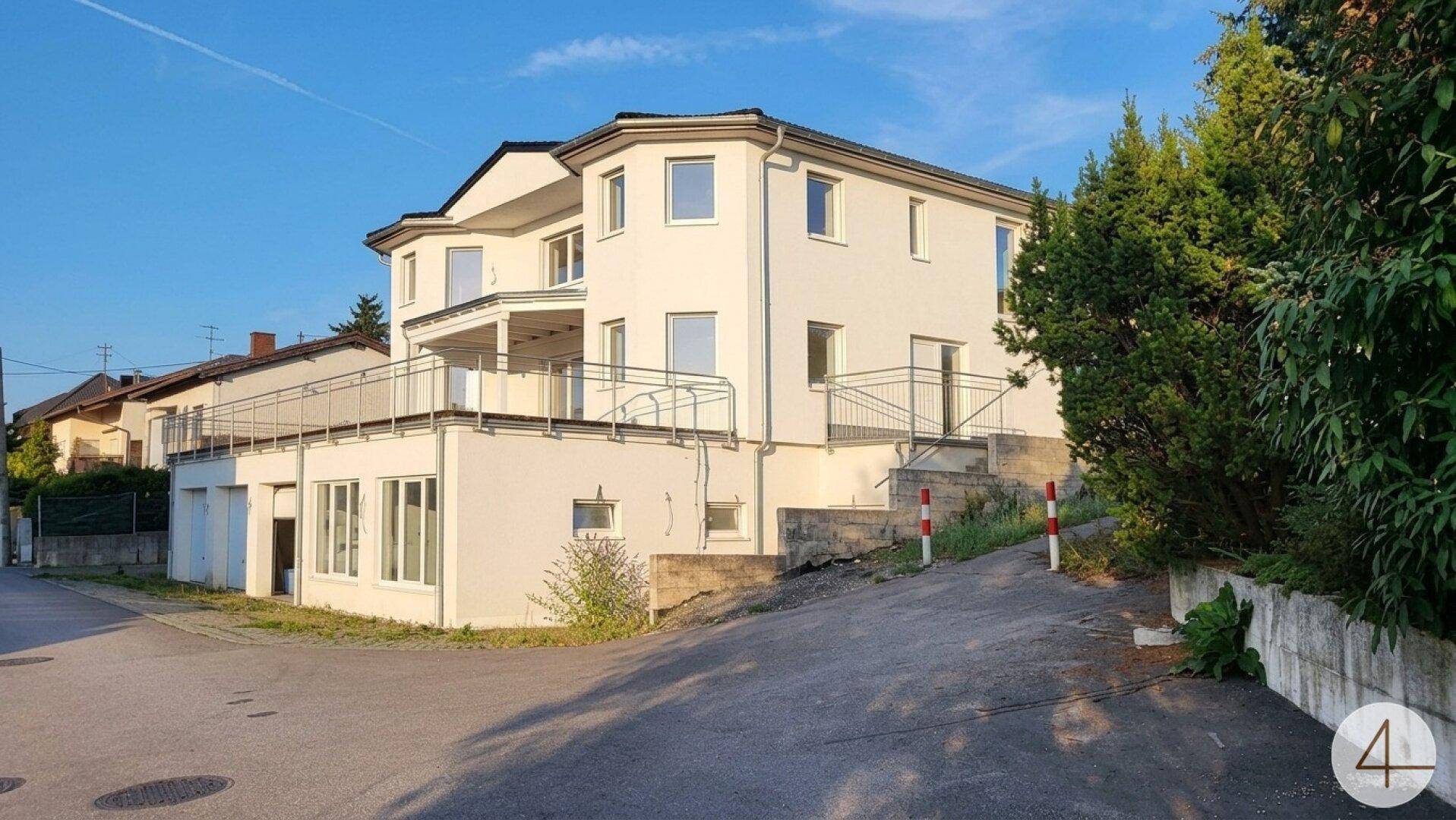 Modernes weißes Gebäude mit mehreren Etagen, großen Fenstern und Balkonen in einer Wohngegend.