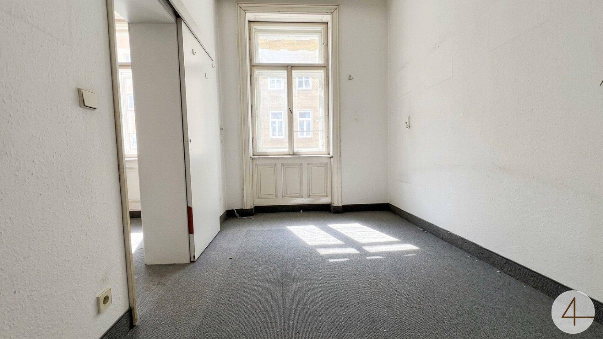 Kleiner, heller Raum mit Teppichboden und einem hohen Fenster, ideal als Schlafzimmer.