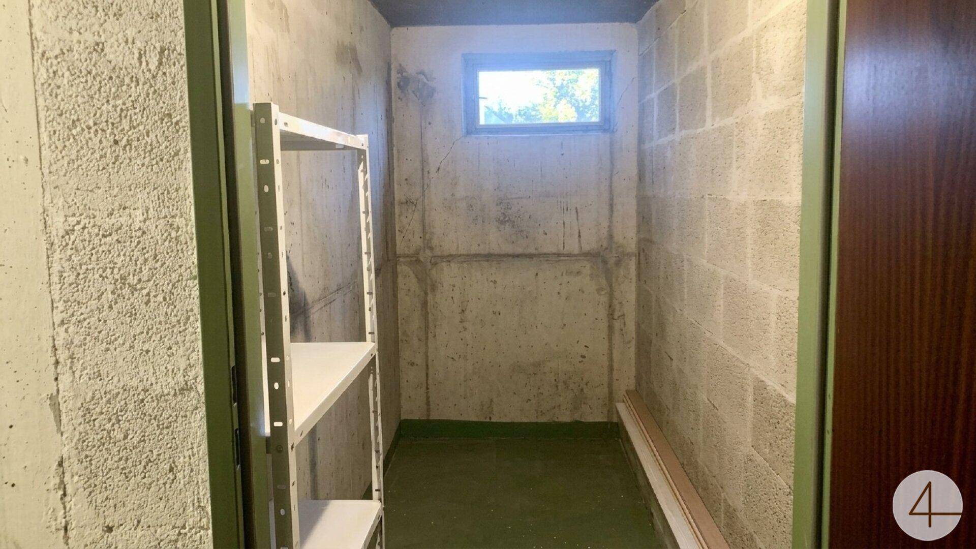 Praktischer Abstellraum mit Betonwänden, kleinem Fenster und Metallregalen für zusätzlichen Stauraum.