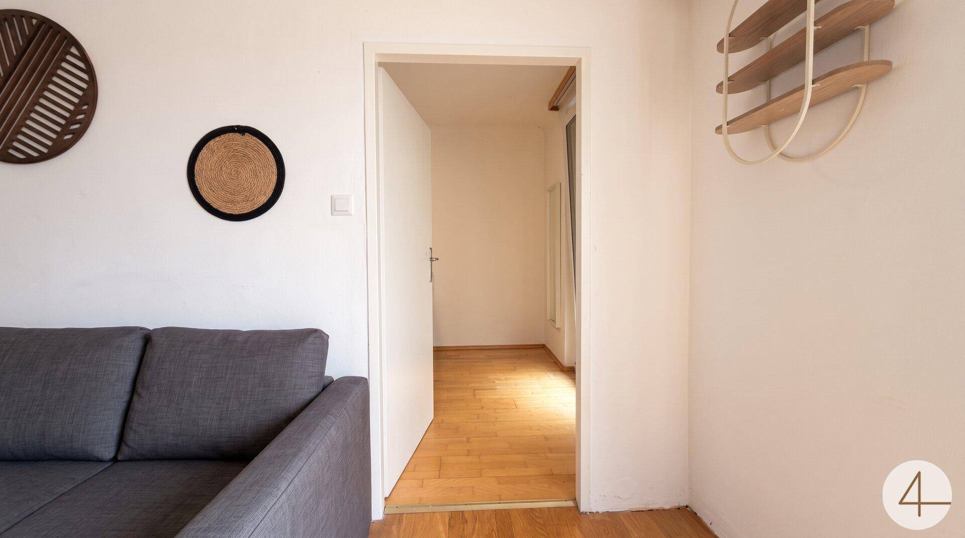 Detailansicht des Wohnbereichs mit bequemer Couch und offenem Durchgang zu einem weiteren Zimmer.
