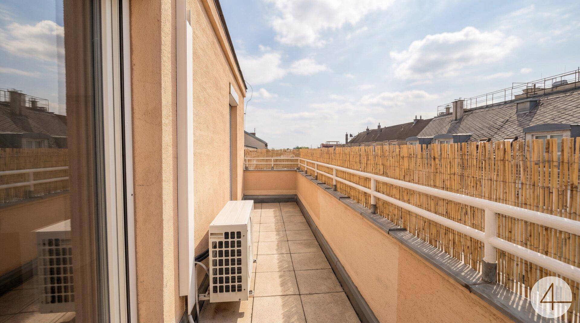 Langer Balkon mit Fliesenboden, Bambusverkleidung und Blick über die Dächer der Stadt.