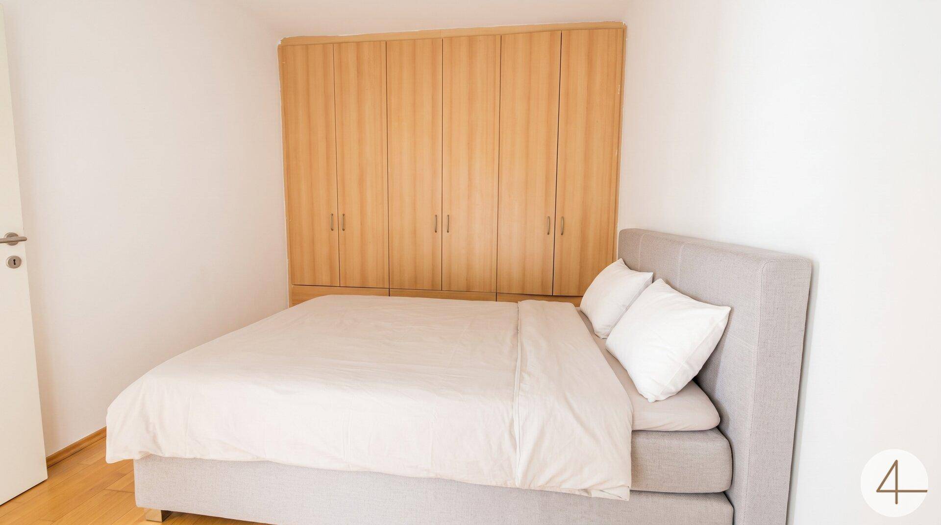 Schlafzimmer mit großem Doppelbett und geräumigem Einbauschrank aus hellem Holz.