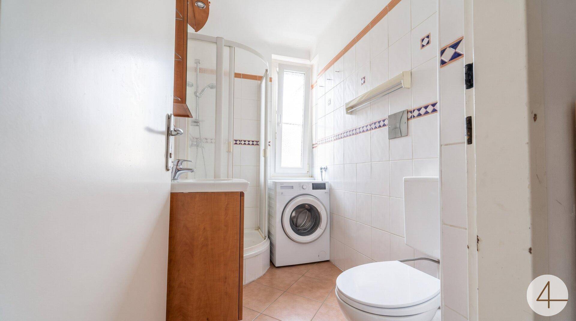 Badezimmer mit Duschkabine, WC, Waschbecken und Waschmaschine, ausgestattet mit Fenster.