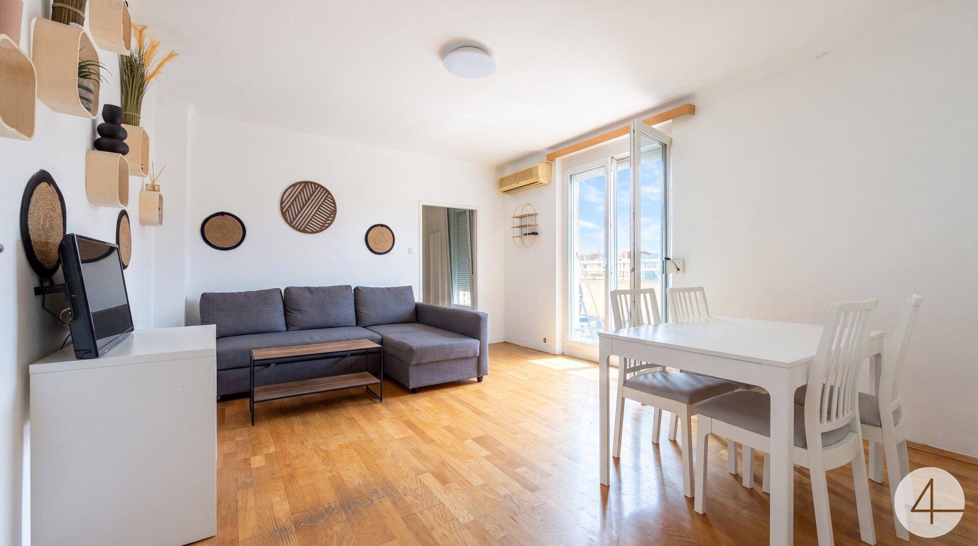 Heller Wohn- und Essbereich mit Holzboden, gemütlichem Sofa und Zugang zum Balkon.