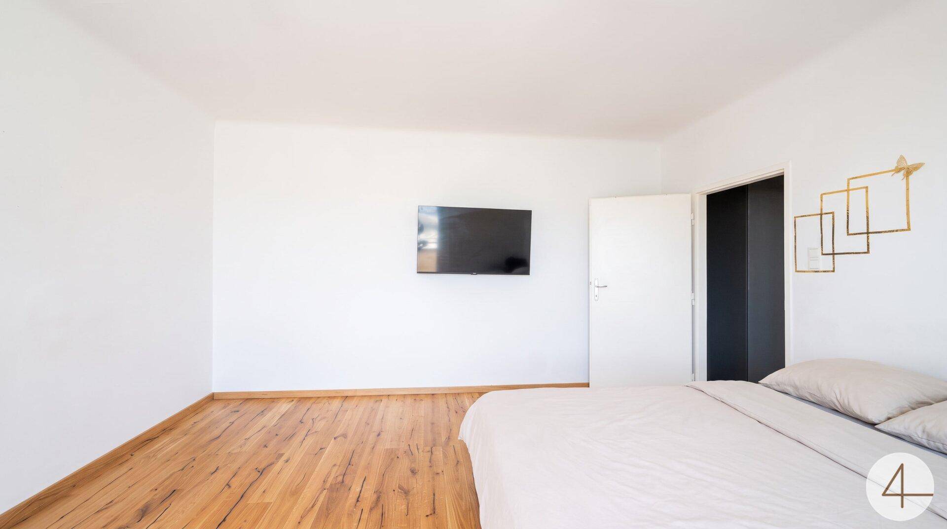 Geräumiges Schlafzimmer mit Holzboden und einem an der Wand montierten Fernseher.