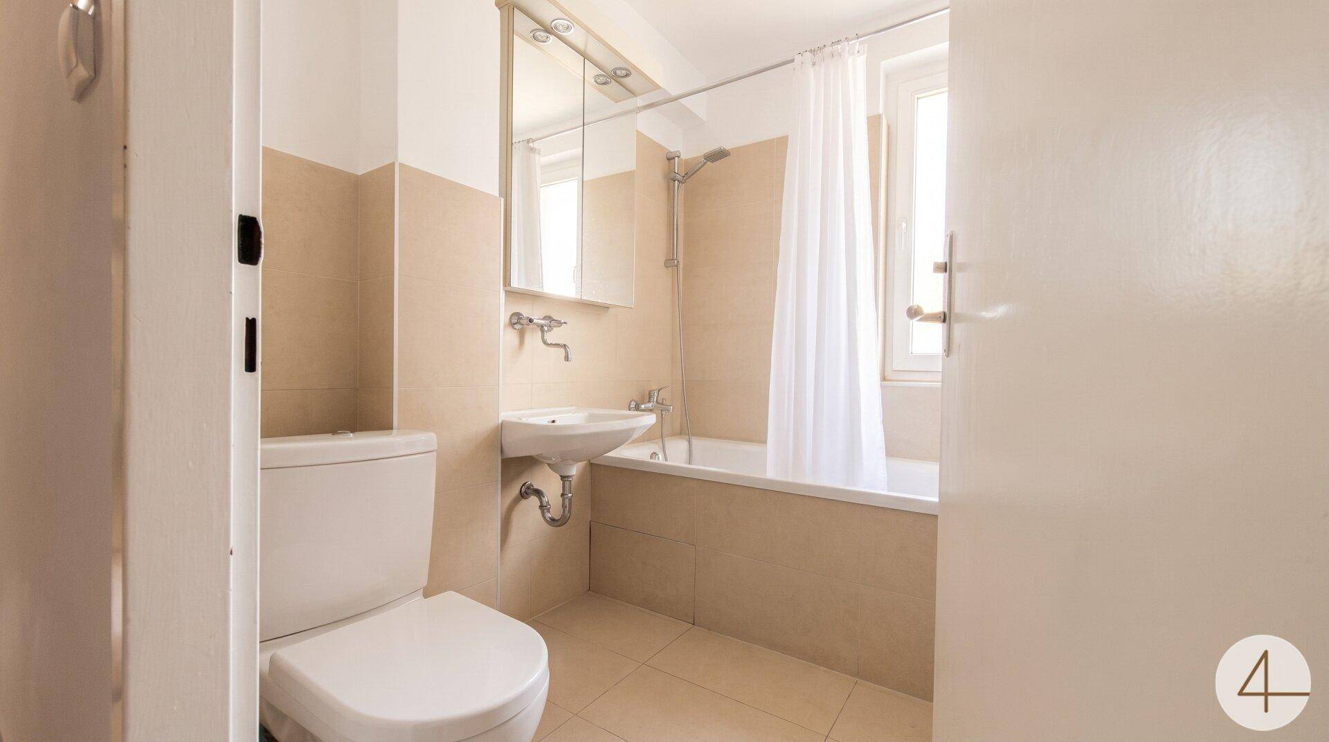Funktionales Badezimmer mit Badewanne, WC, Waschbecken und einem Fenster für Tageslicht.