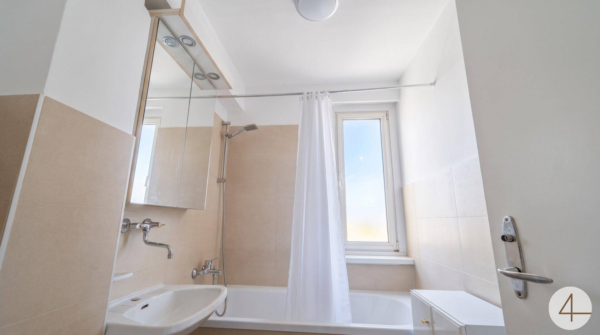 Helles Badezimmer mit Badewanne, Duschvorhang und einem Fenster für natürliche Belüftung.