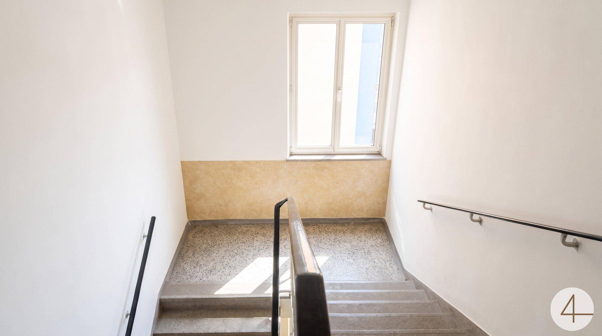 Helles Treppenhaus mit Fenster und robustem Bodenbelag, der viel Licht hereinlässt.