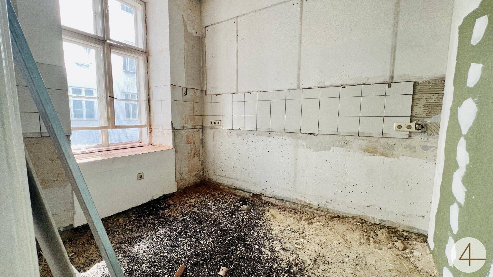 Küche im Rohbauzustand mit Fenster und vorbereiteten Fliesen für den Spritzschutz, bereit für Einbau.