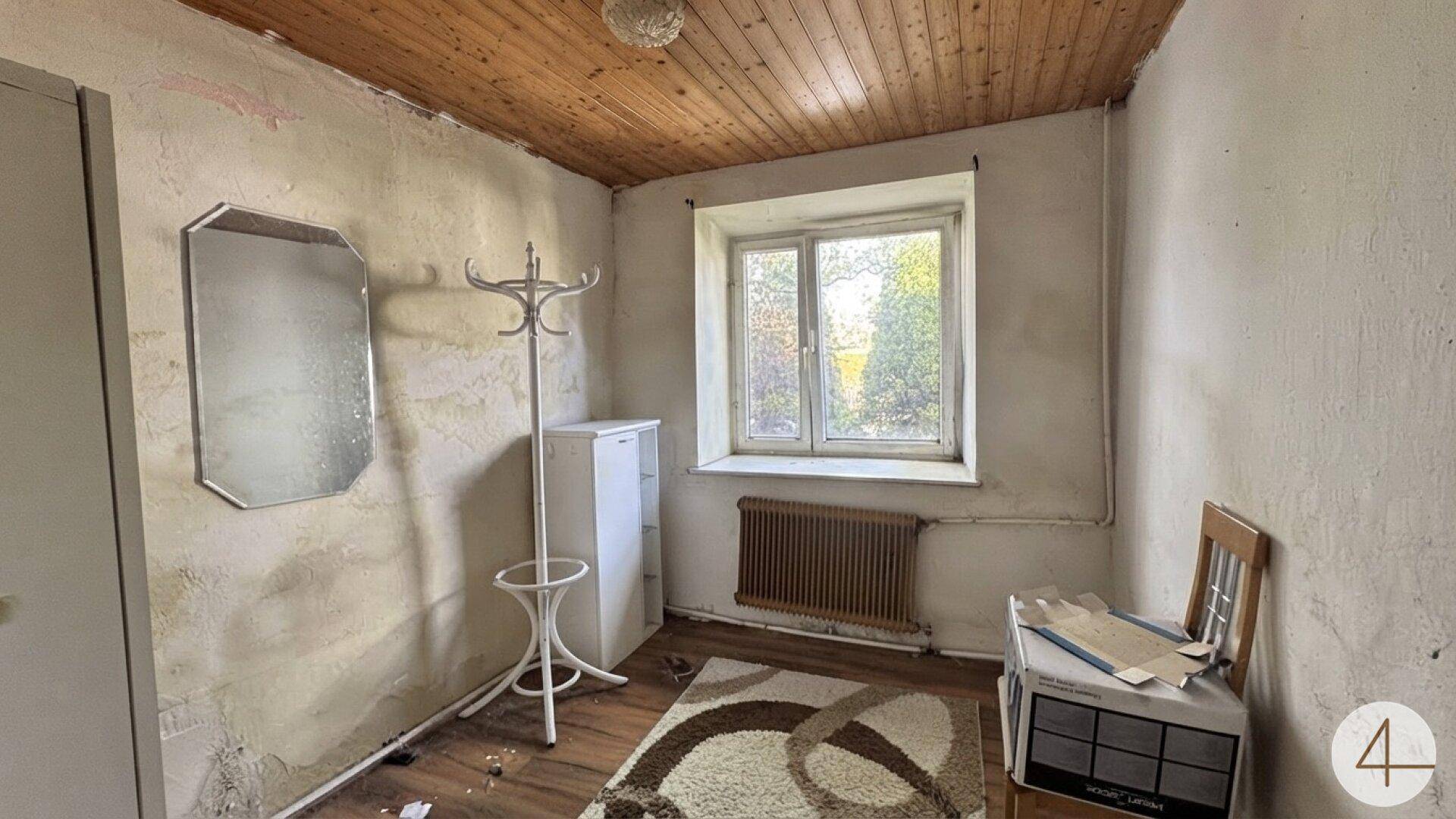 Kleines Zimmer mit Holzdecke, alten Tapeten und einem Fenster mit Blick ins Grüne.
