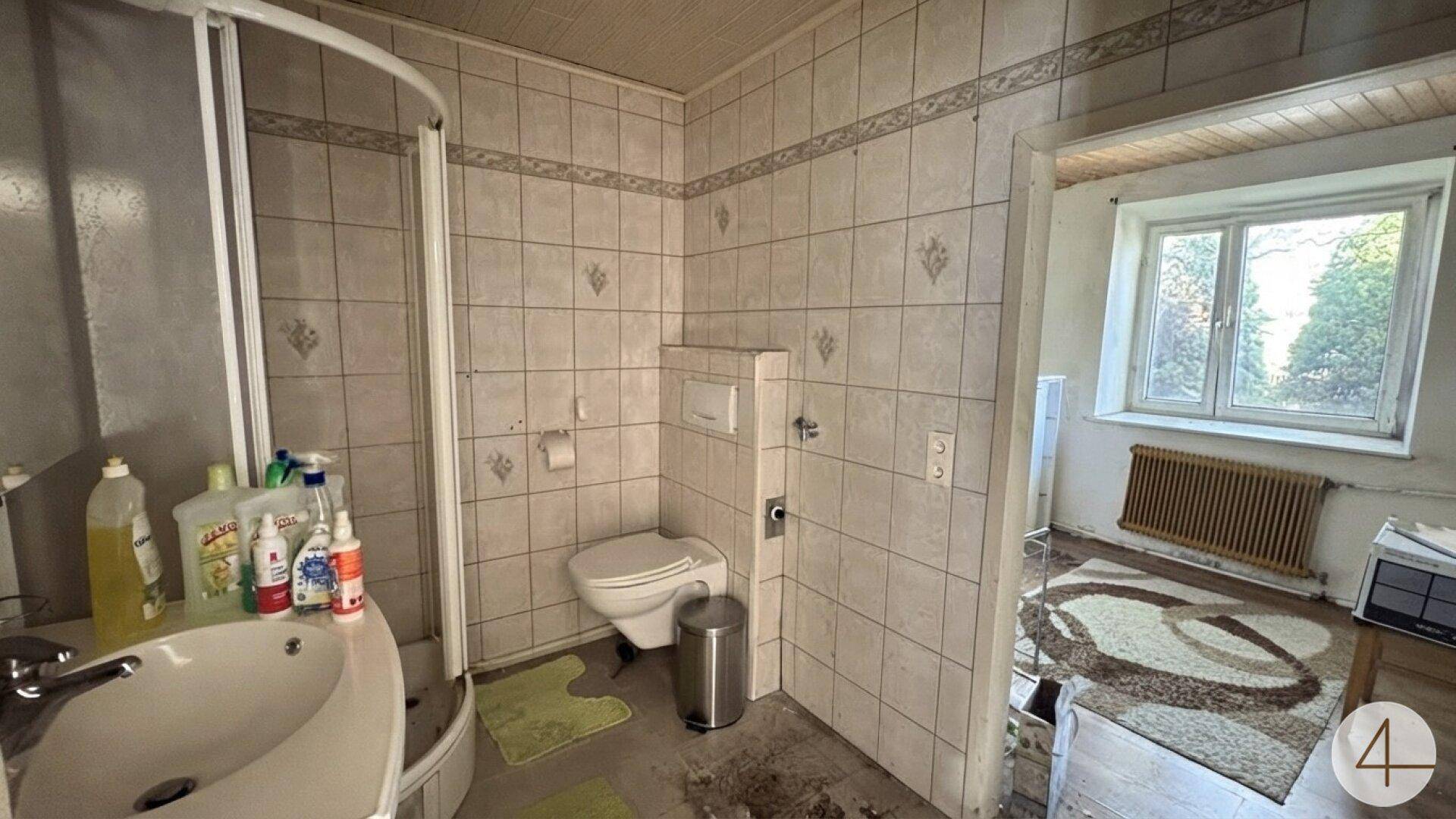 Gefliestes Badezimmer mit Duschkabine, Toilette und Waschbecken, renovierungsbedürftig.