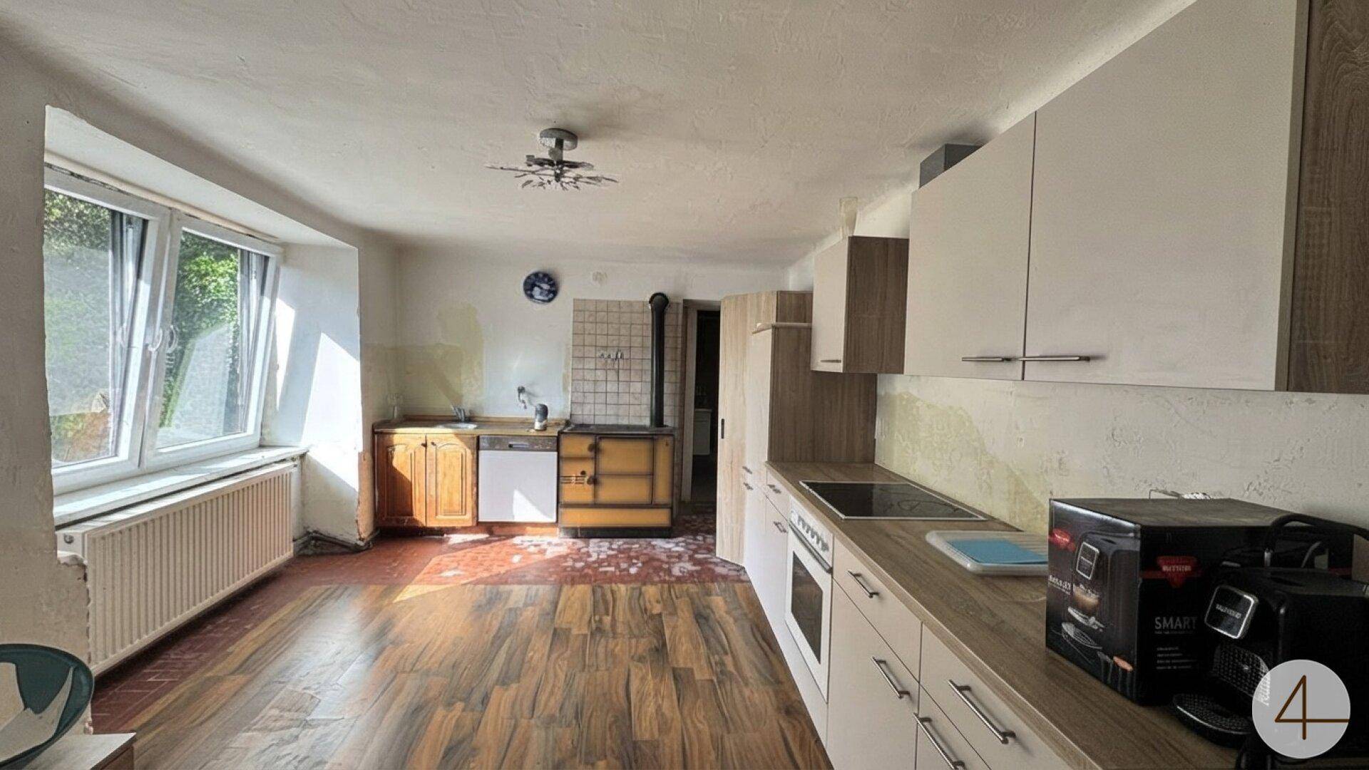 Küche mit Holzboden, teilweise modernen Schränken und einem traditionellen Holzofen.