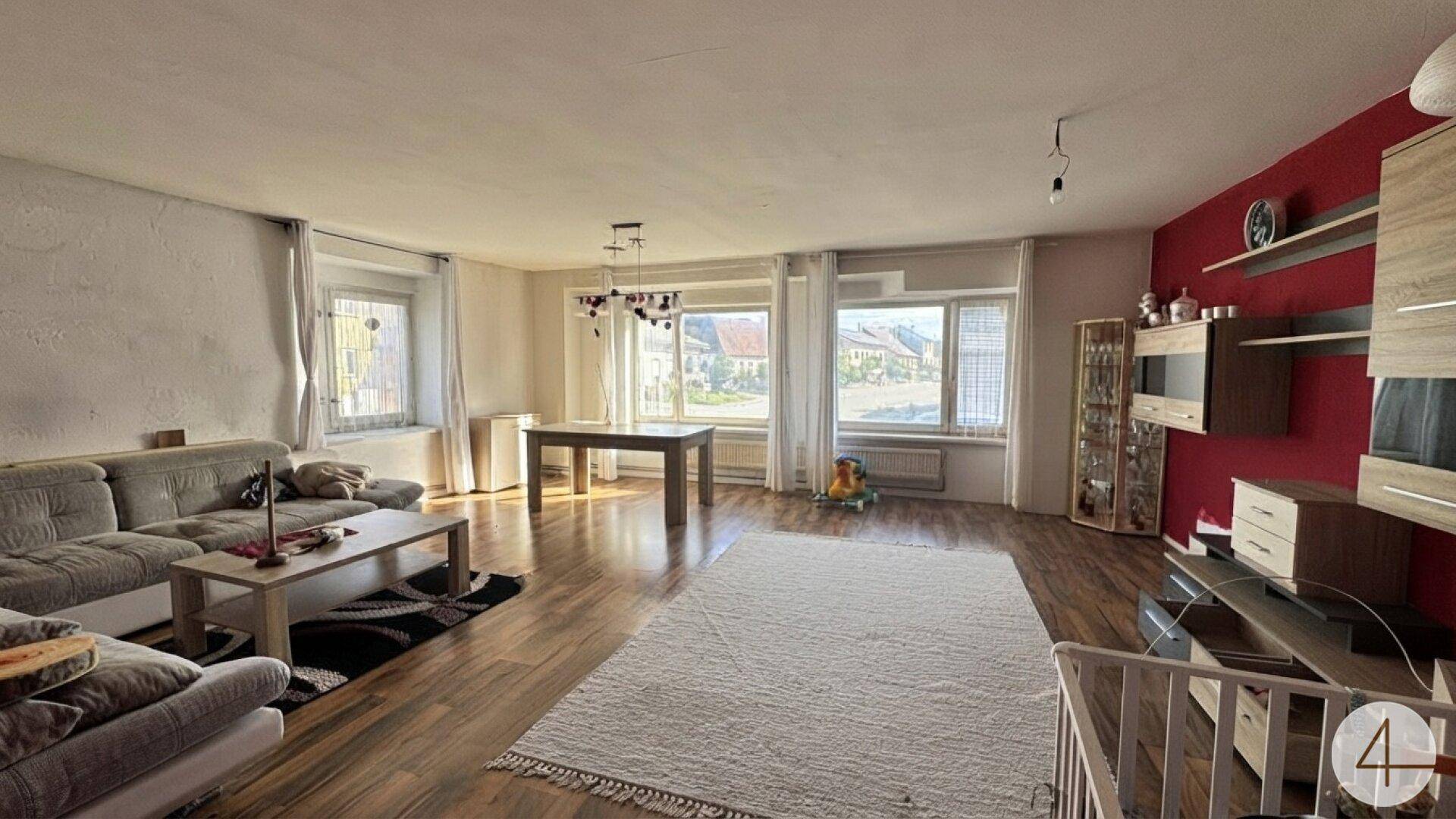 Geräumiger Wohn-Essbereich mit Holzboden, Sofa und Esstisch, hell durch große Fenster.