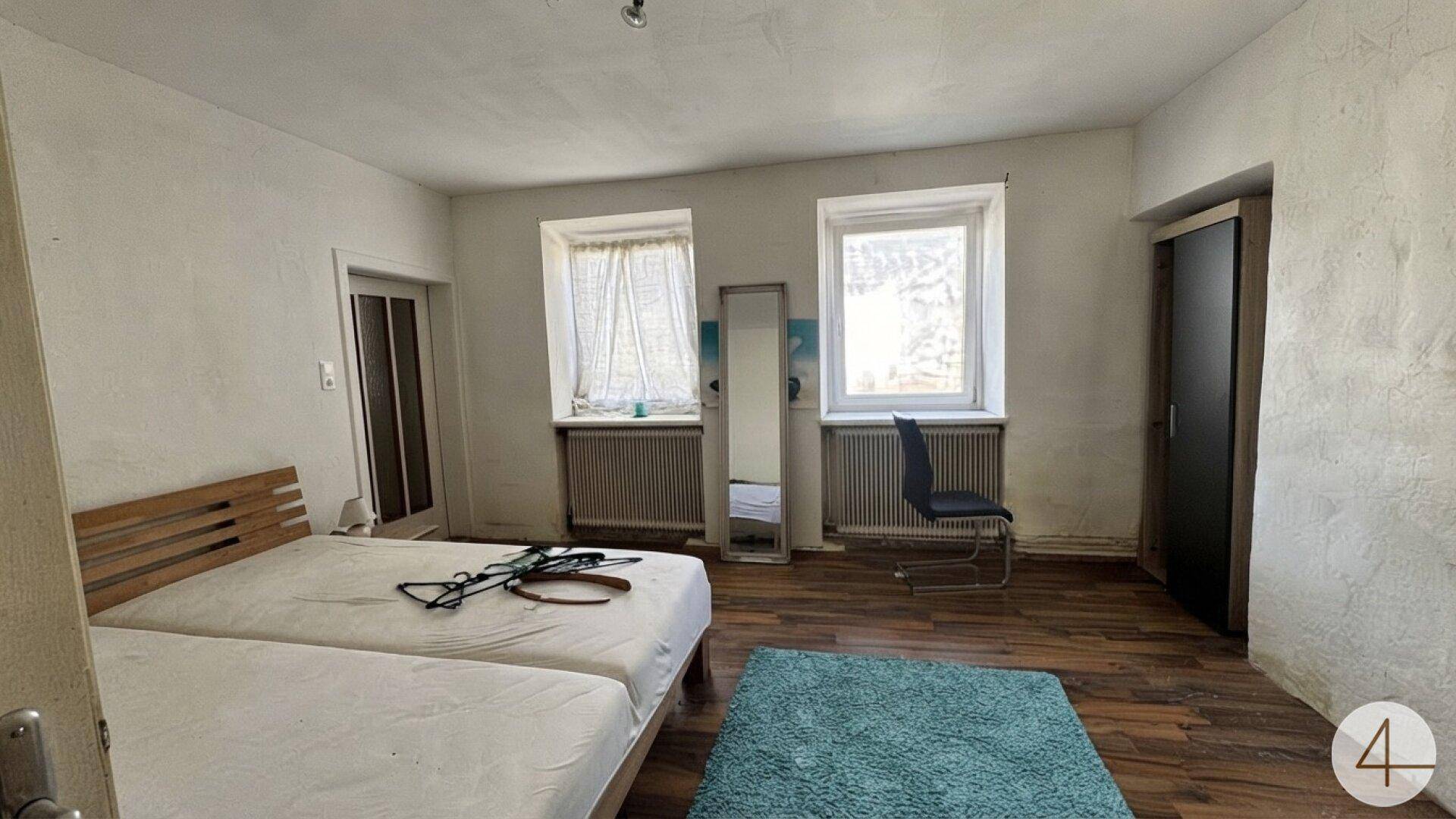 Schlafzimmer mit Holzboden, zwei Einzelbetten und Fenstern mit Heizkörpern darunter.