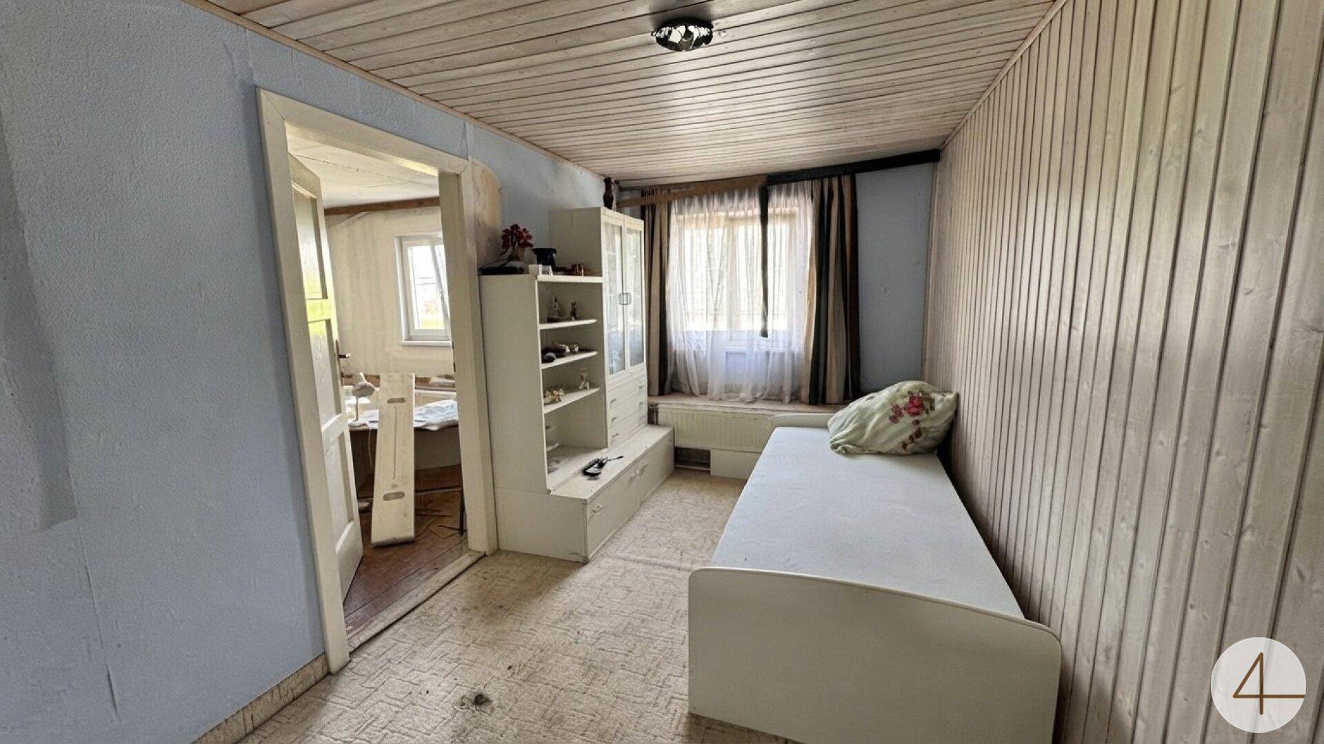 Kleines Zimmer mit Holzvertäfelung an Wänden und Decke, ausgestattet mit einem Einzelbett.