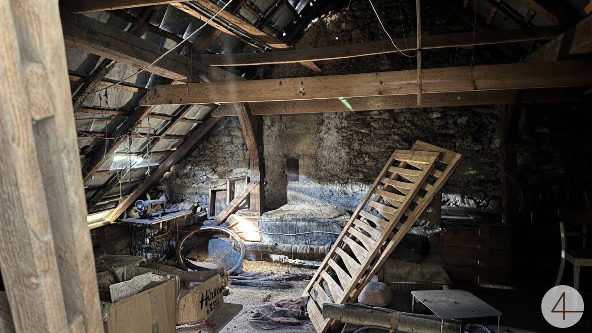 Dachboden mit freiliegenden Holzbalken und Steinmauern, genutzt als Abstellraum.