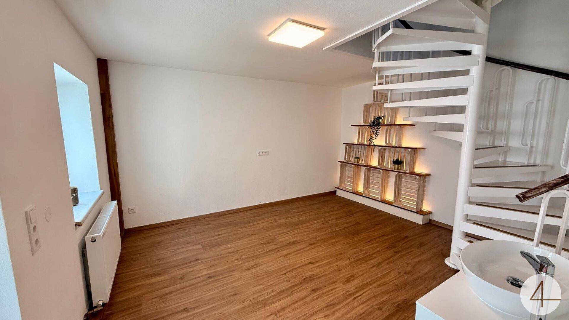 Heller Raum mit Holzfußboden, einer Wendeltreppe und einer dekorativen Regalwand.