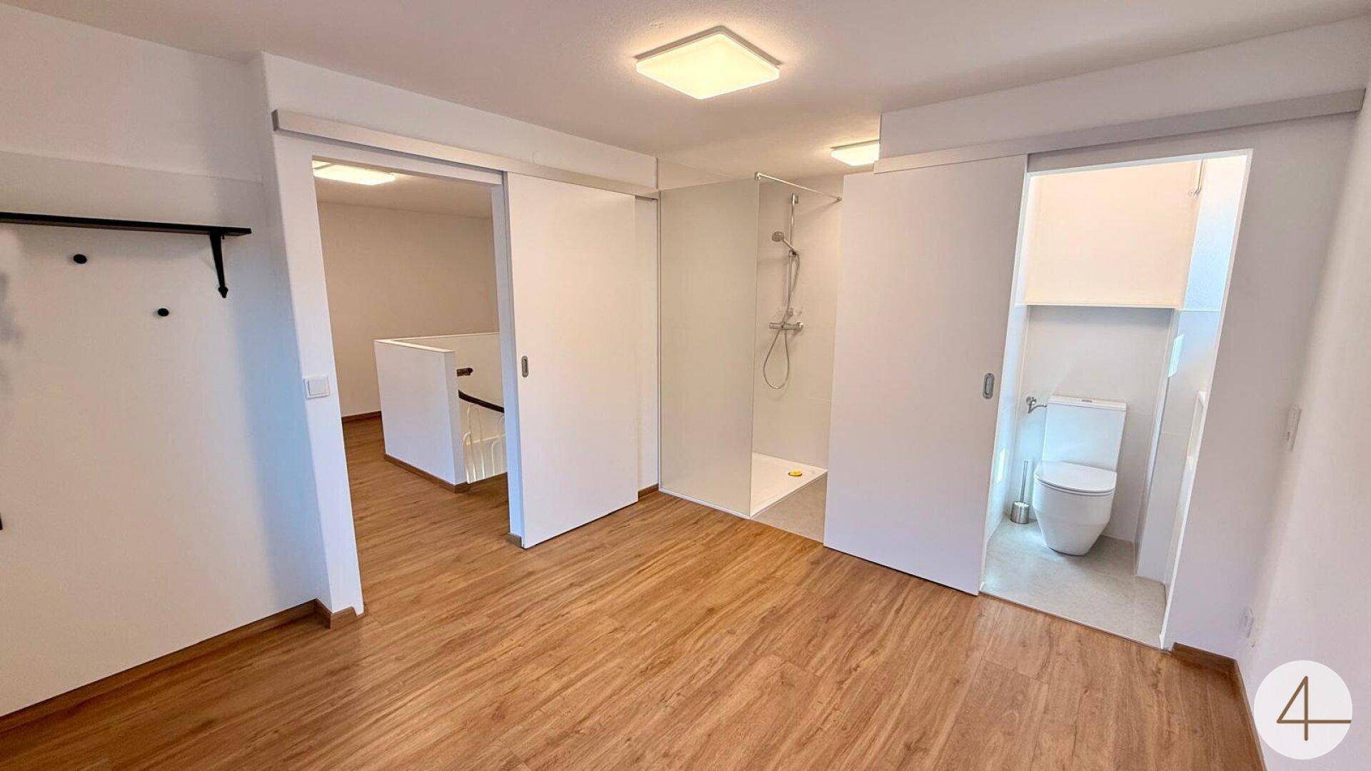 Offener Bereich mit Holzfußboden, Schiebetüren zu Dusche und Toilette sowie einem weiteren Raum.
