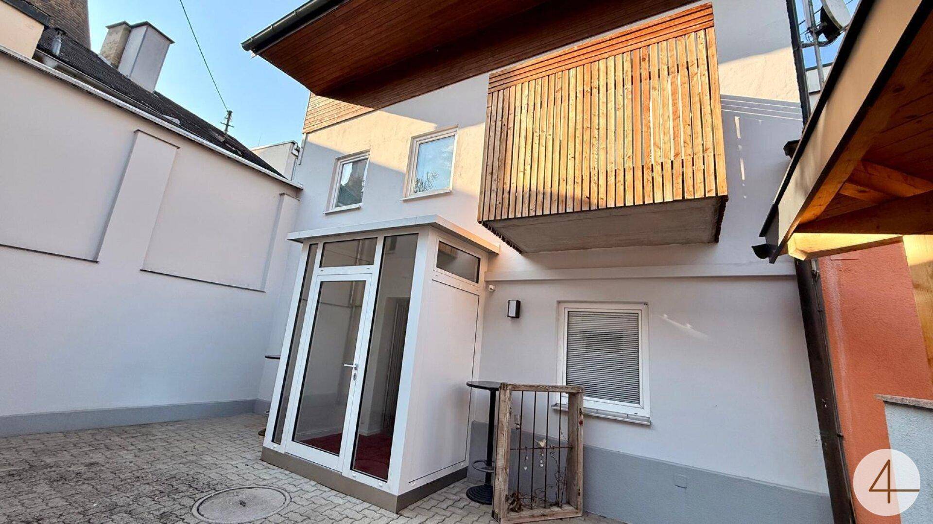 Gebäudefassade mit einem verglasten Eingangsbereich und einem Holzbalkon im oberen Stockwerk.