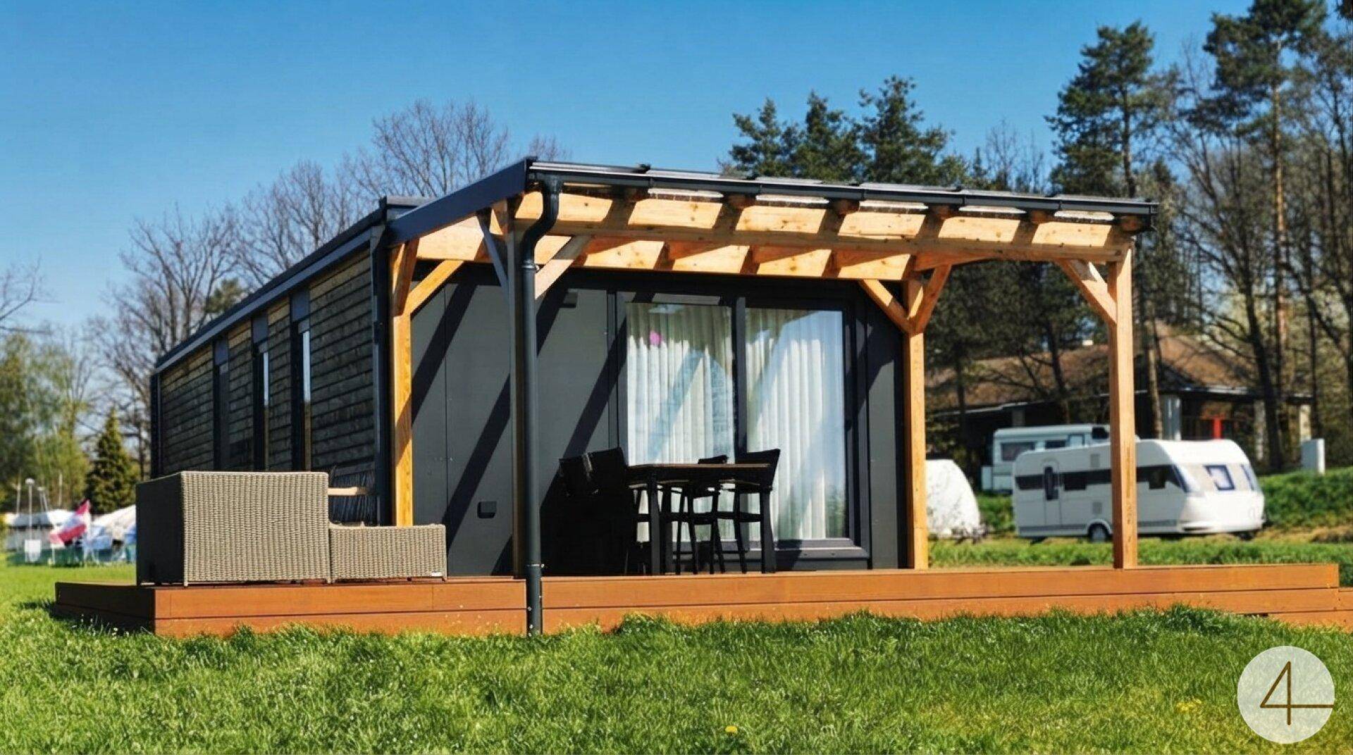 Seitliche Ansicht der modularen Unterkunft mit Holzterrasse und Gartenmöbeln.