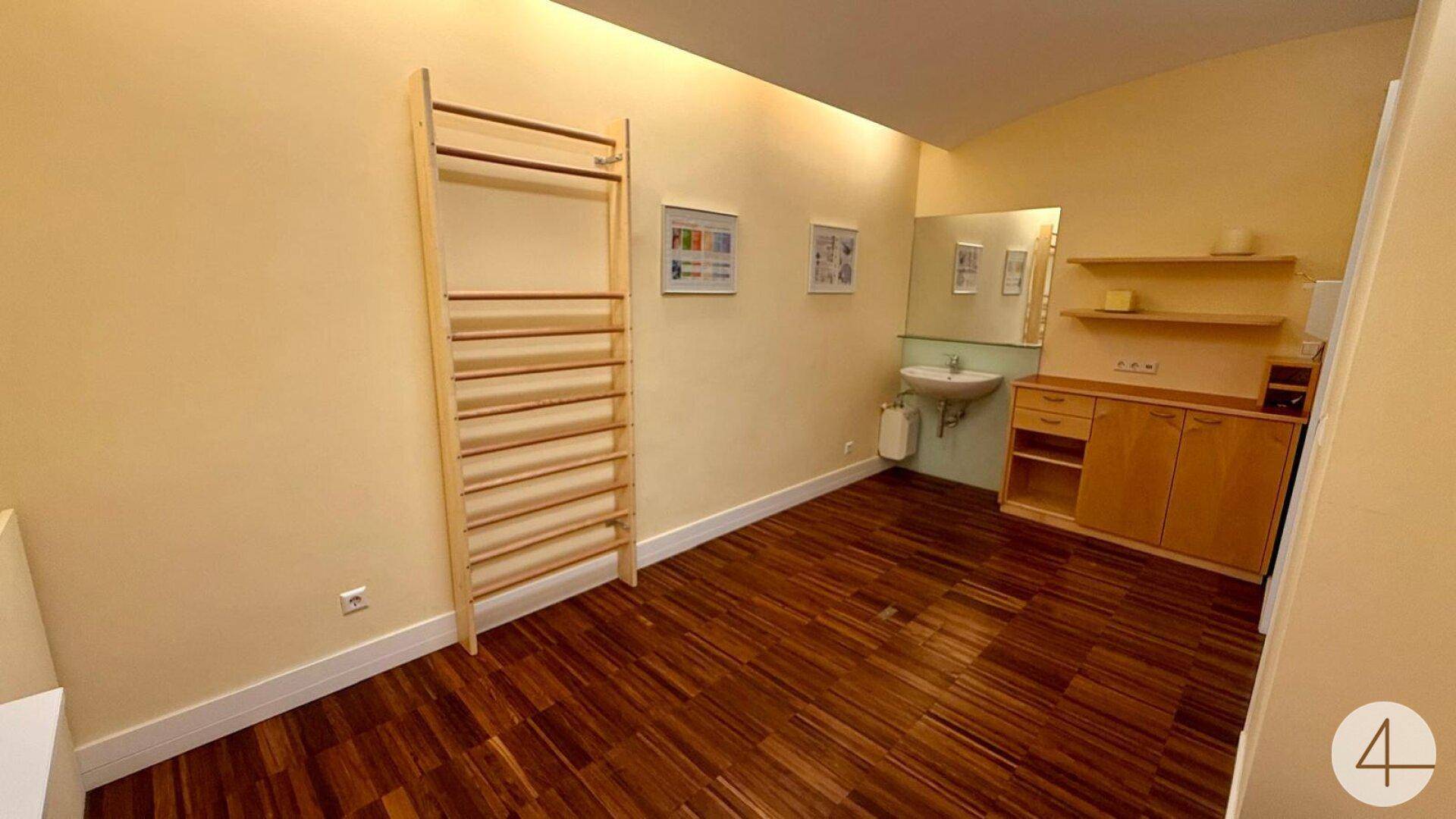 Heller Raum mit Holzfußboden, Sprossenwand und Waschbeckenbereich, ideal für Therapie oder Büro.