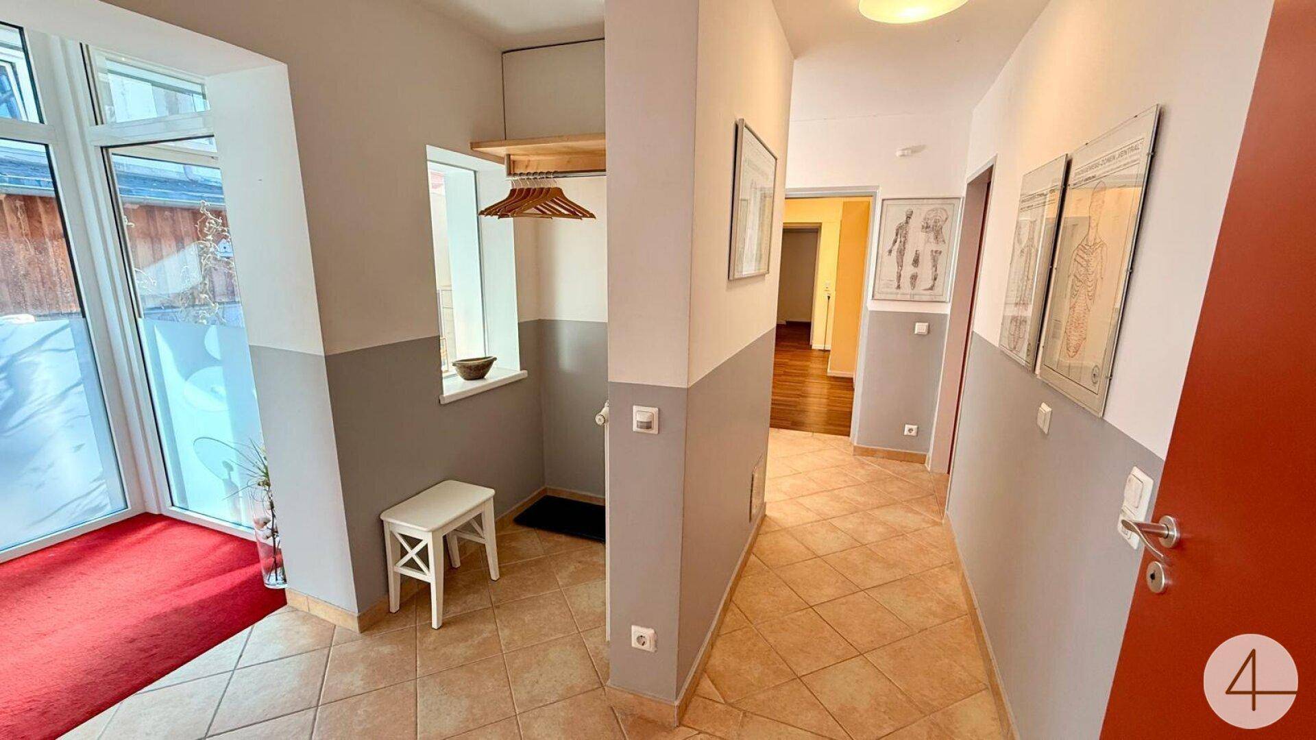 Eingangsbereich mit Fliesenboden, Garderobe und Glastür, die zum Außenbereich führt.