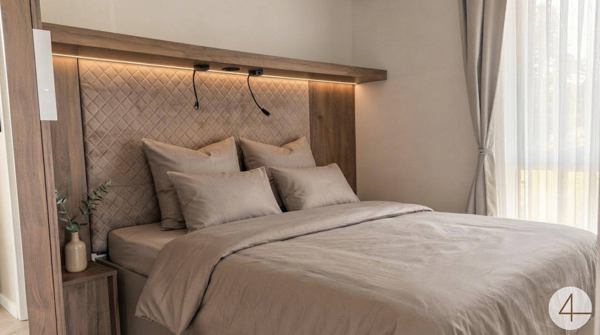 Gemütliches Schlafzimmer mit gepolstertem Kopfteil, indirekter Beleuchtung und beigefarbener Bettwäsche.