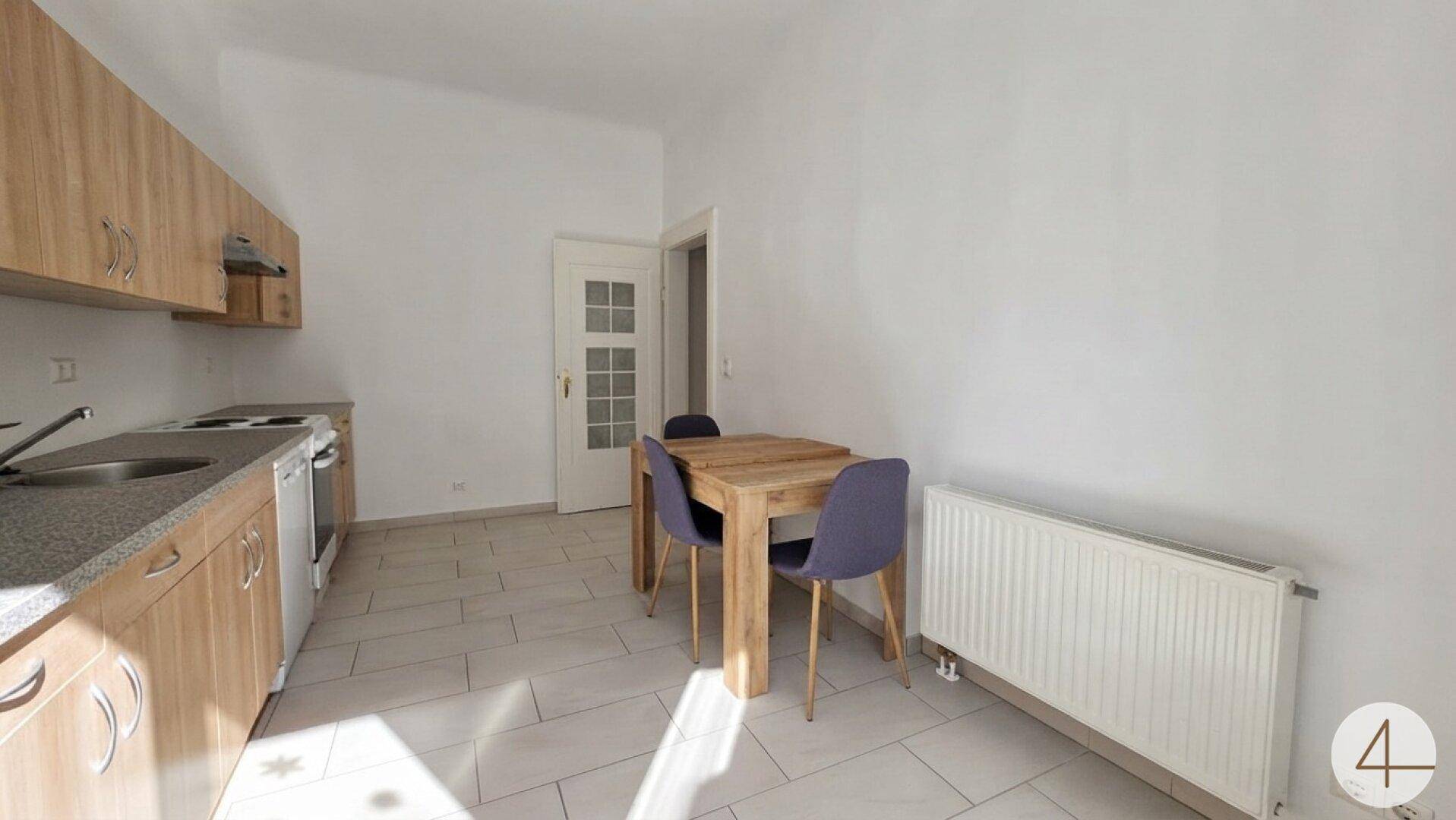 Funktionale Küche mit hellen Holzschränken, Esstisch und Fliesenboden, ideal für Mahlzeiten.