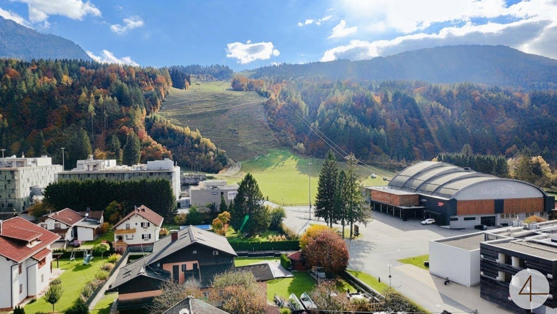 Weitläufiger Blick auf die Berglandschaft mit Wäldern, einer Skipiste und umliegenden Gebäuden.