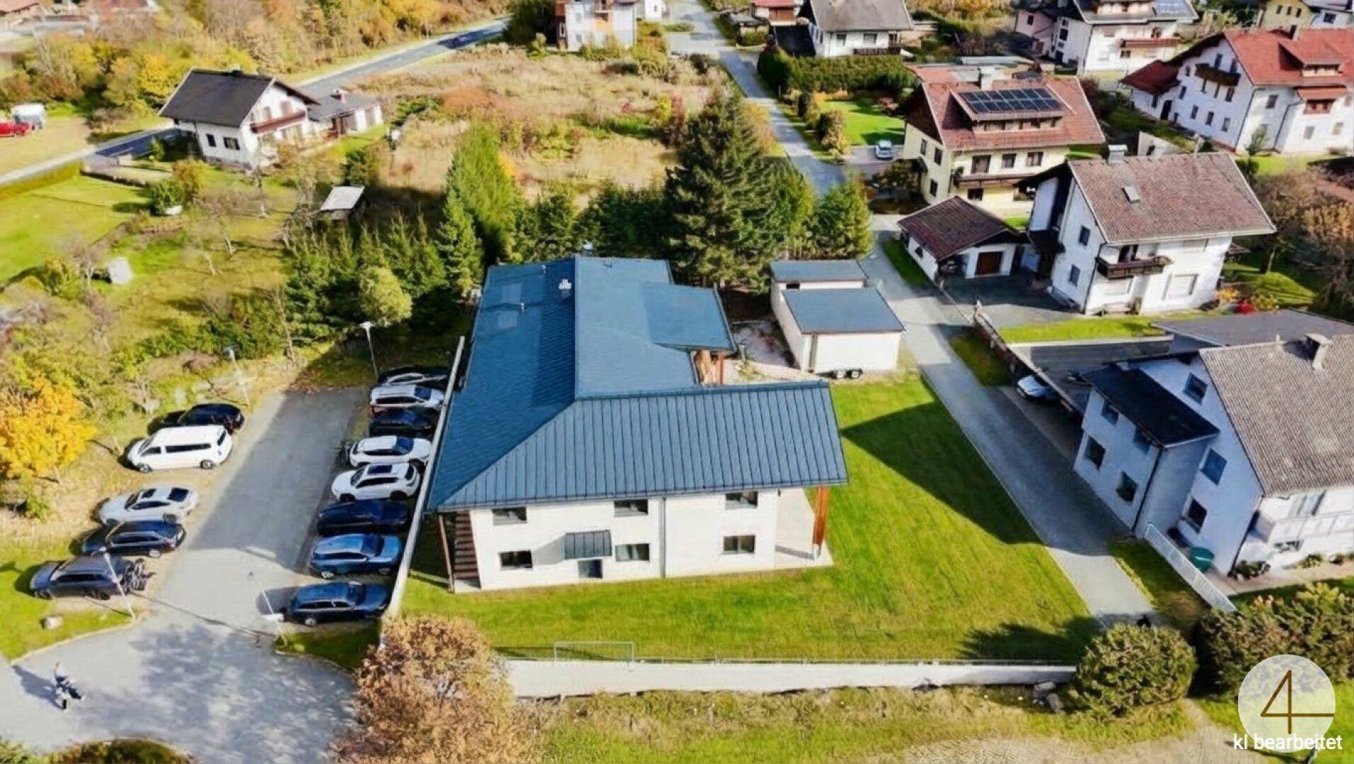 Luftaufnahme des Hauses von der Seite, mit Parkplätzen und angrenzenden Wohnhäusern in ländlicher Umgebung.