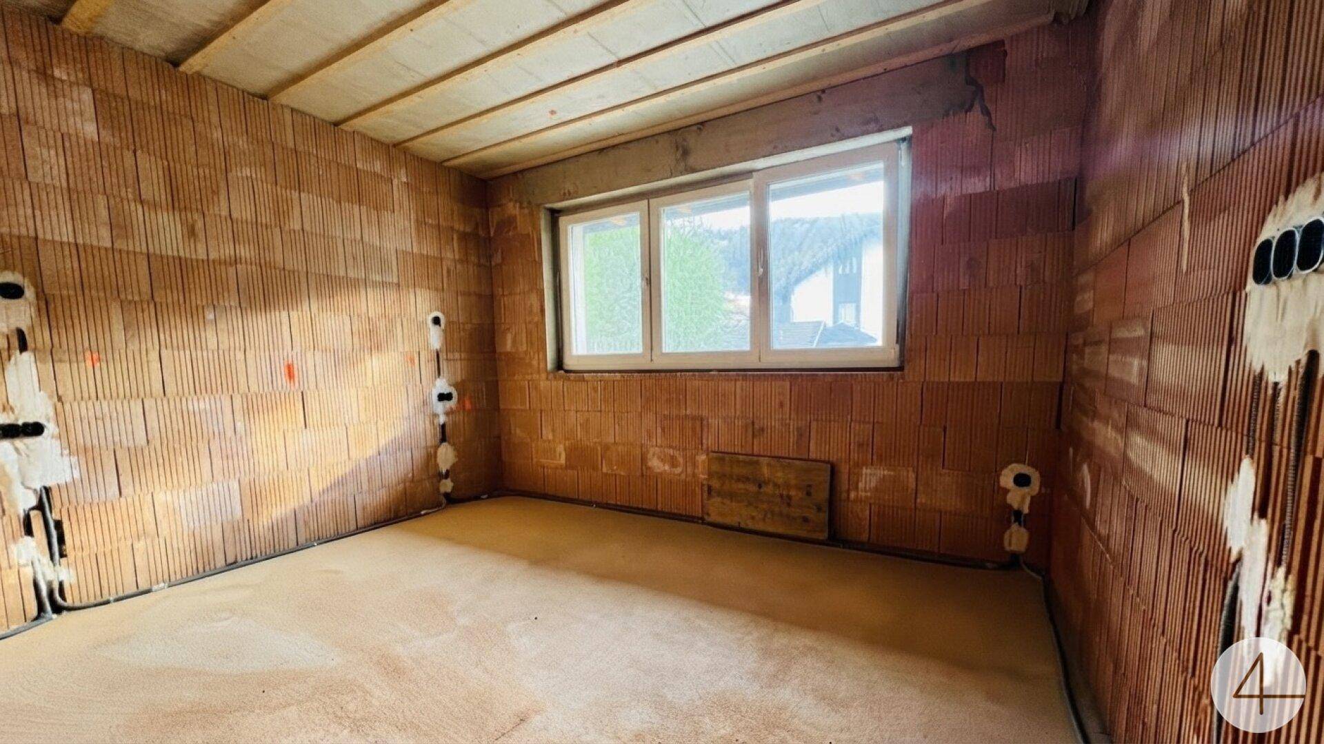 Rohbauzimmer mit Ziegelwänden, sichtbaren Installationen und einem Fenster, bereit für den Innenausbau.