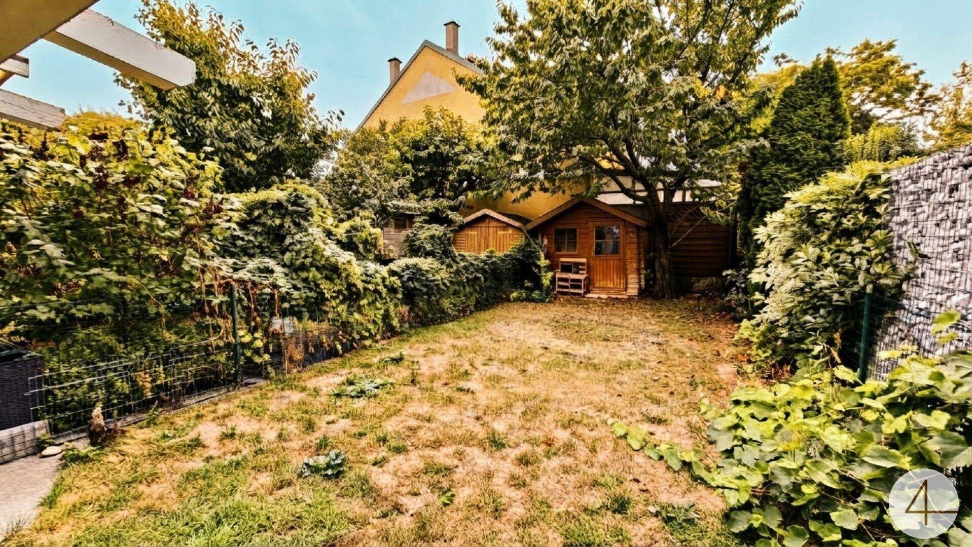 Grüner Garten mit Rasenfläche, alten Bäumen und zwei Gartenhäuschen.