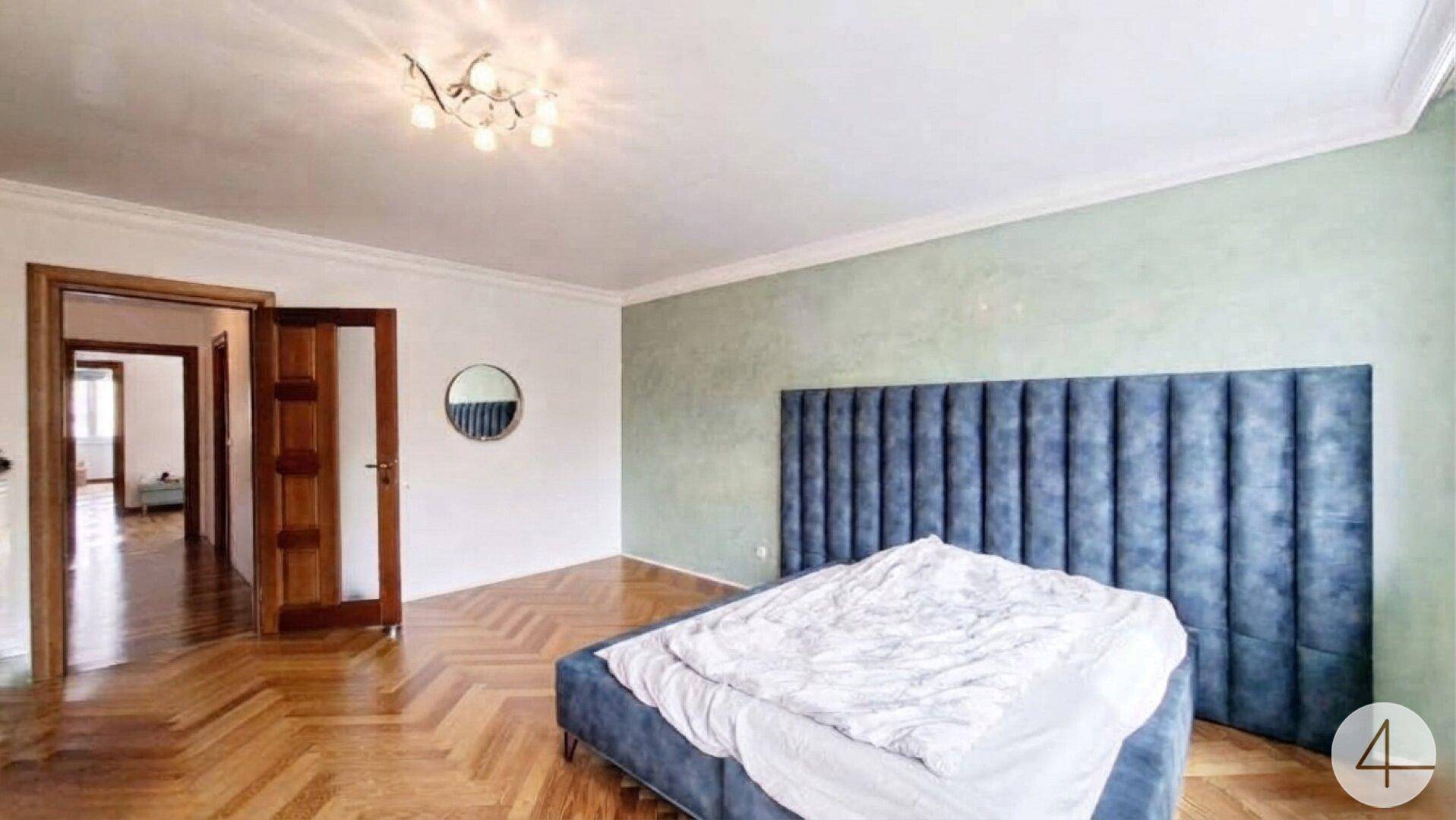 Schlafzimmer mit Fischgrätparkett, blauem Bett und hellgrüner Akzentwand.
