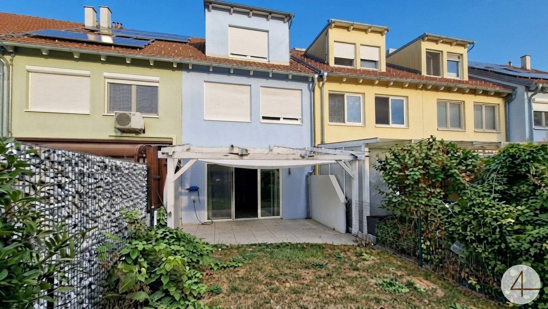 Hinterhof mit kleiner Rasenfläche, Terrasse unter einer Pergola und Zugang zum Haus.