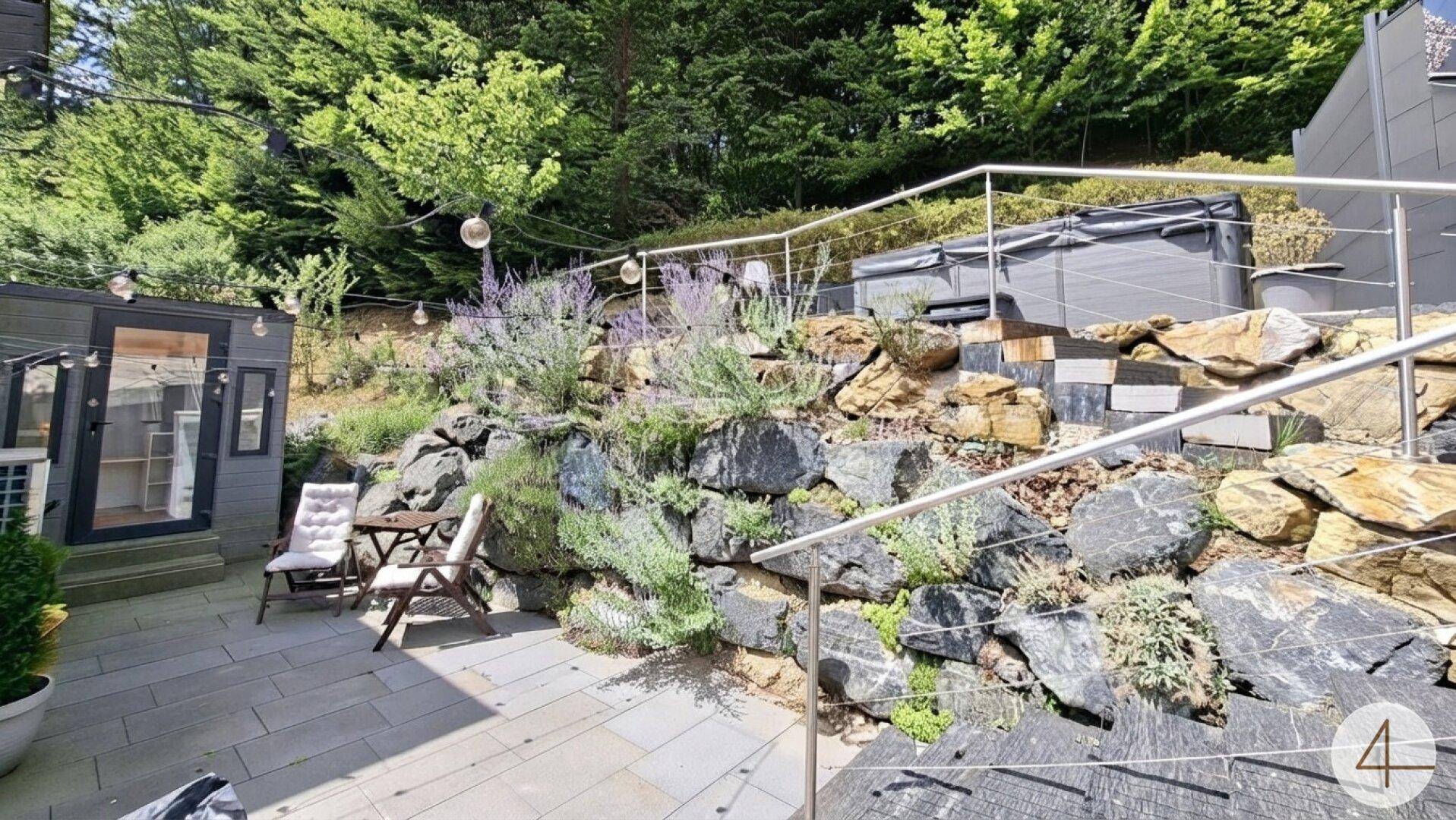 Große Terrasse mit Sitzbereich, Steingarten und Zugang zu einem Whirlpool, umgeben von viel Grün.