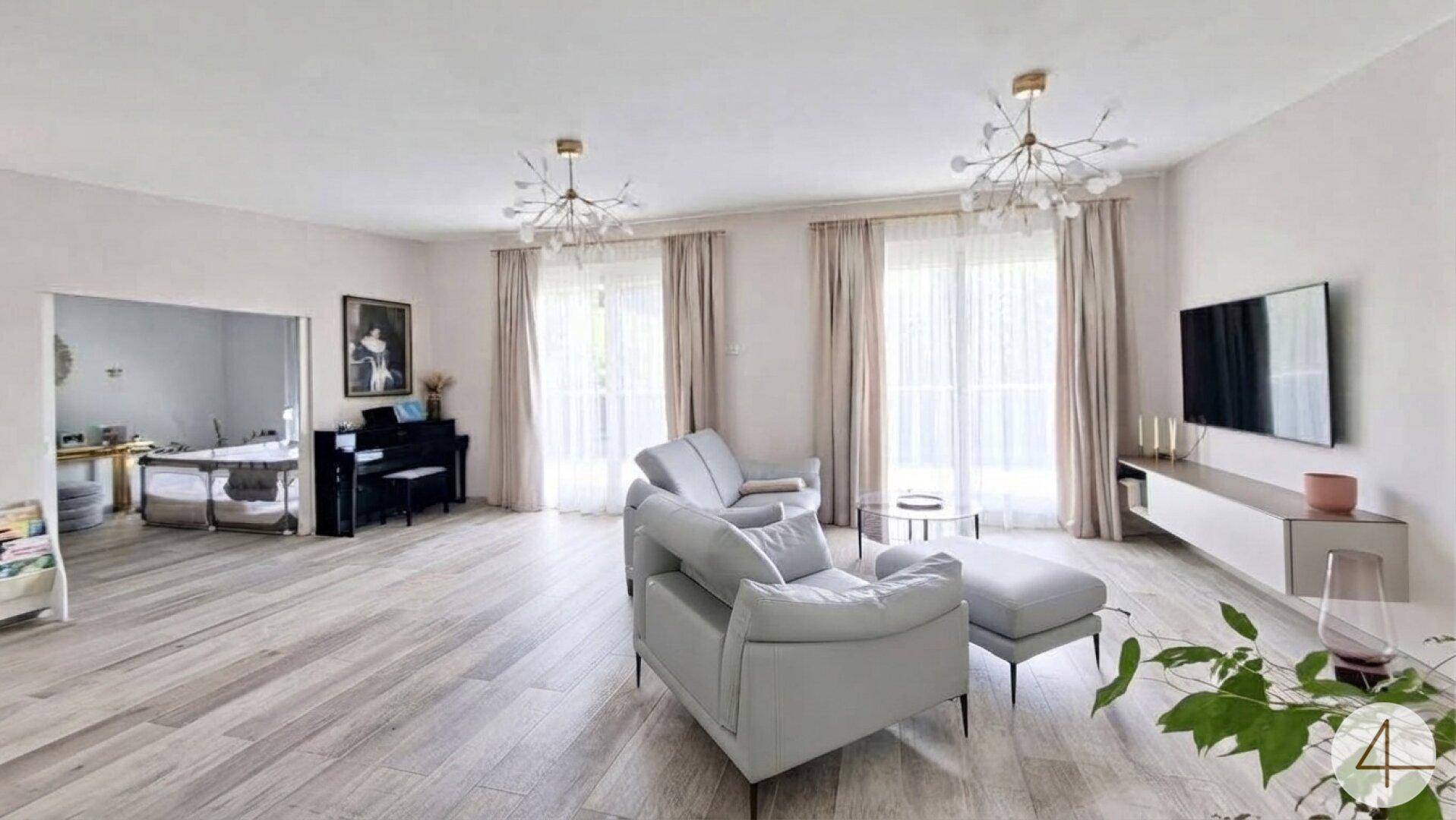 Helles Wohnzimmer mit großen Fenstern, bequemen Sofas und einem modernen TV-Bereich.