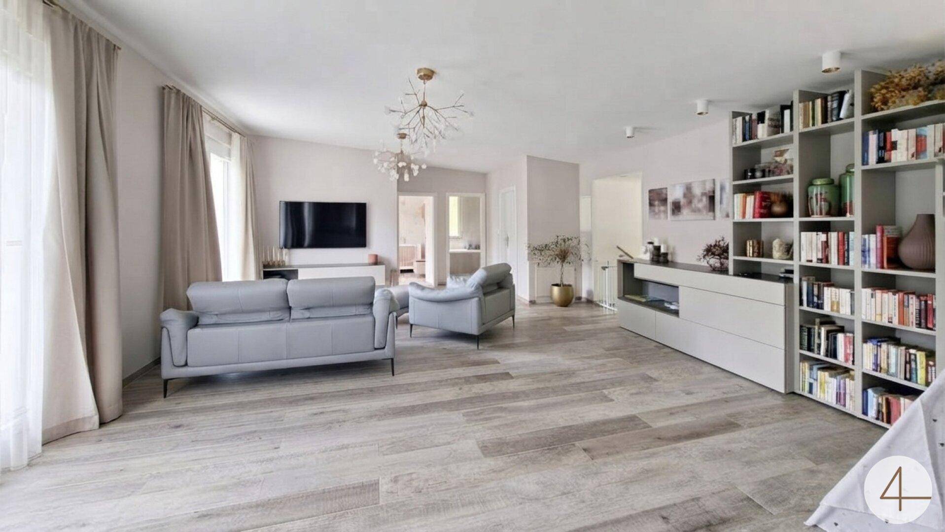 Geräumiges Wohnzimmer mit umfangreichem Bücherregal, modernen Sofas und hellem Bodenbelag.