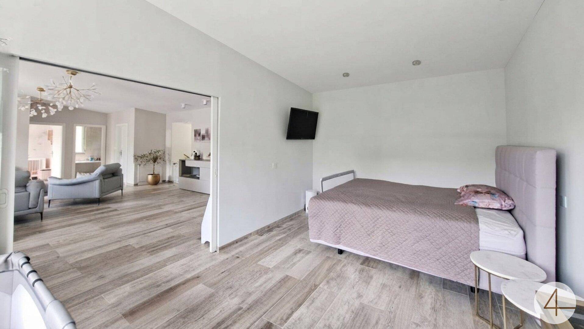 Schlafzimmer mit modernem Bett, Wandfernseher und Schiebetüren zum angrenzenden Wohnbereich.