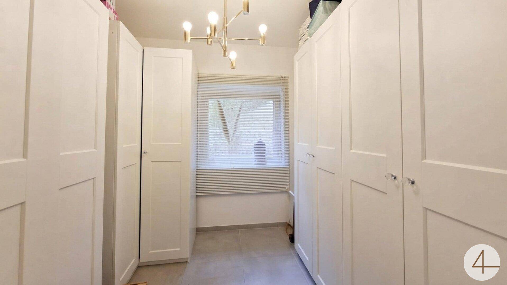 Ankleidezimmer mit weißen Einbauschränken und Fenster für natürliches Licht.