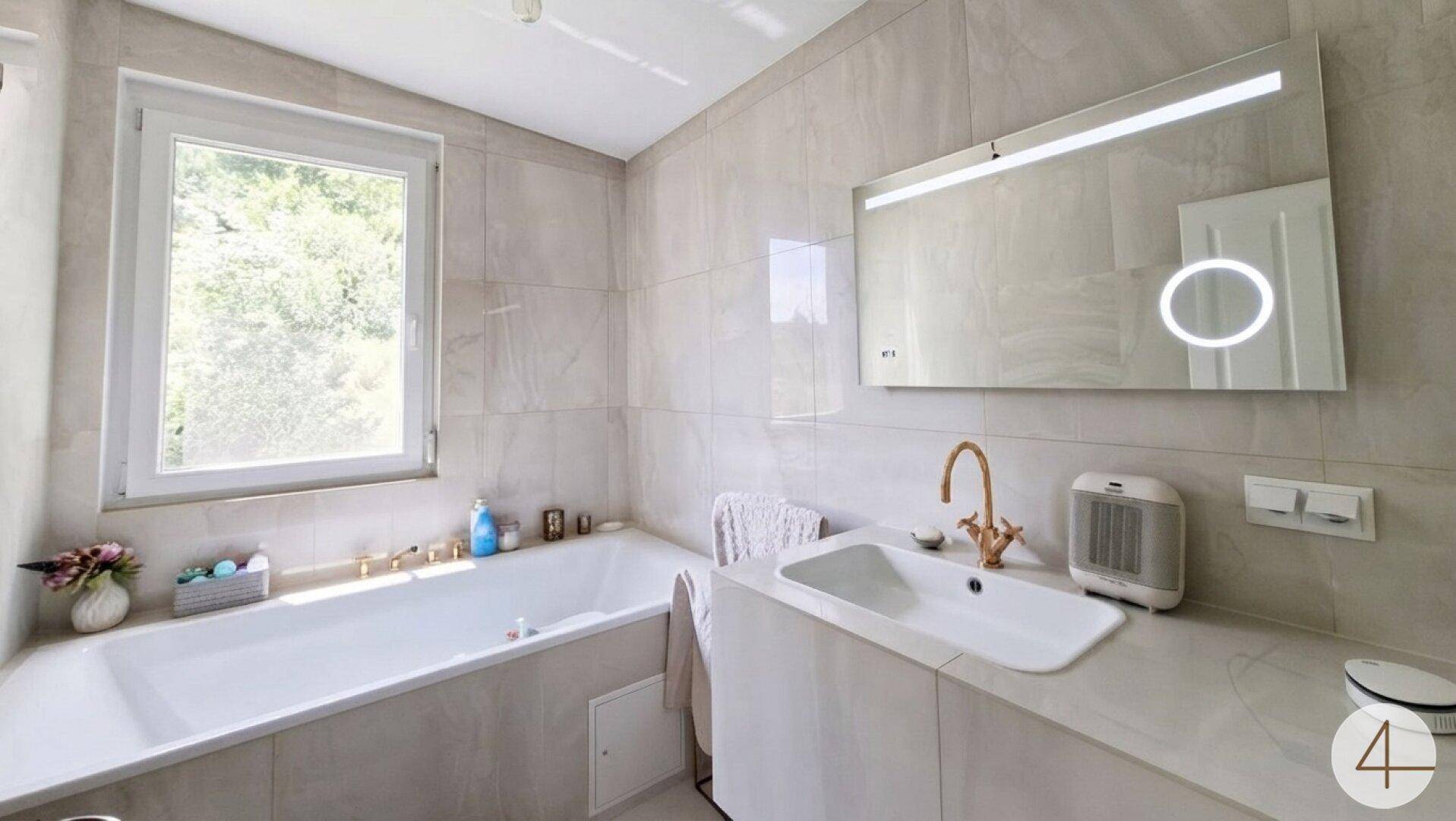 Helles Badezimmer mit Badewanne, modernem Waschbecken und Fenster für Tageslicht.
